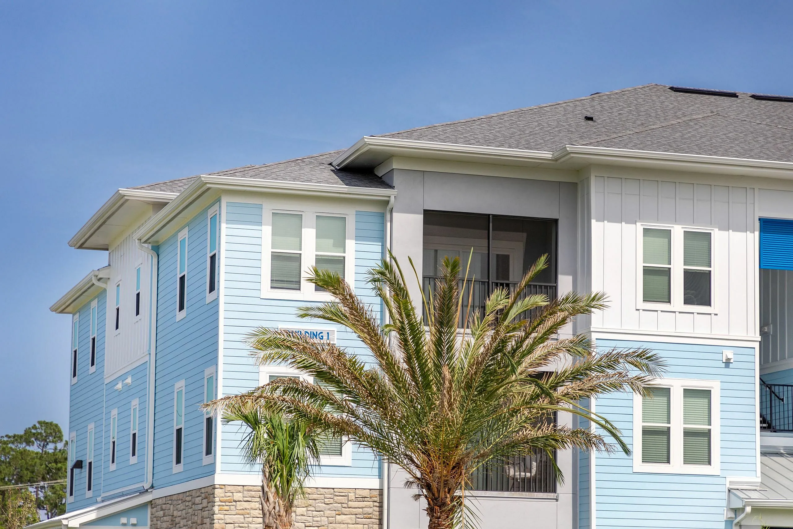 Charming coastal apartment building with sky-blue siding, modern architecture, and tropical palm trees.