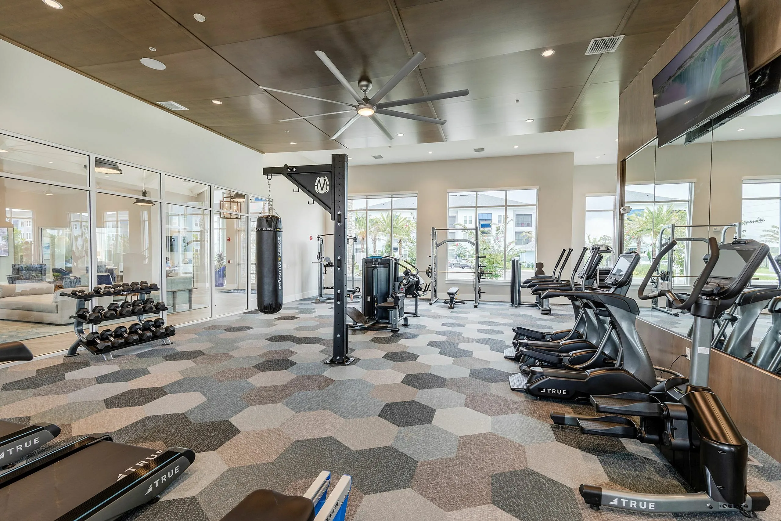 Modern fitness center with state-of-the-art equipment, boxing bag, and natural light through large windows.