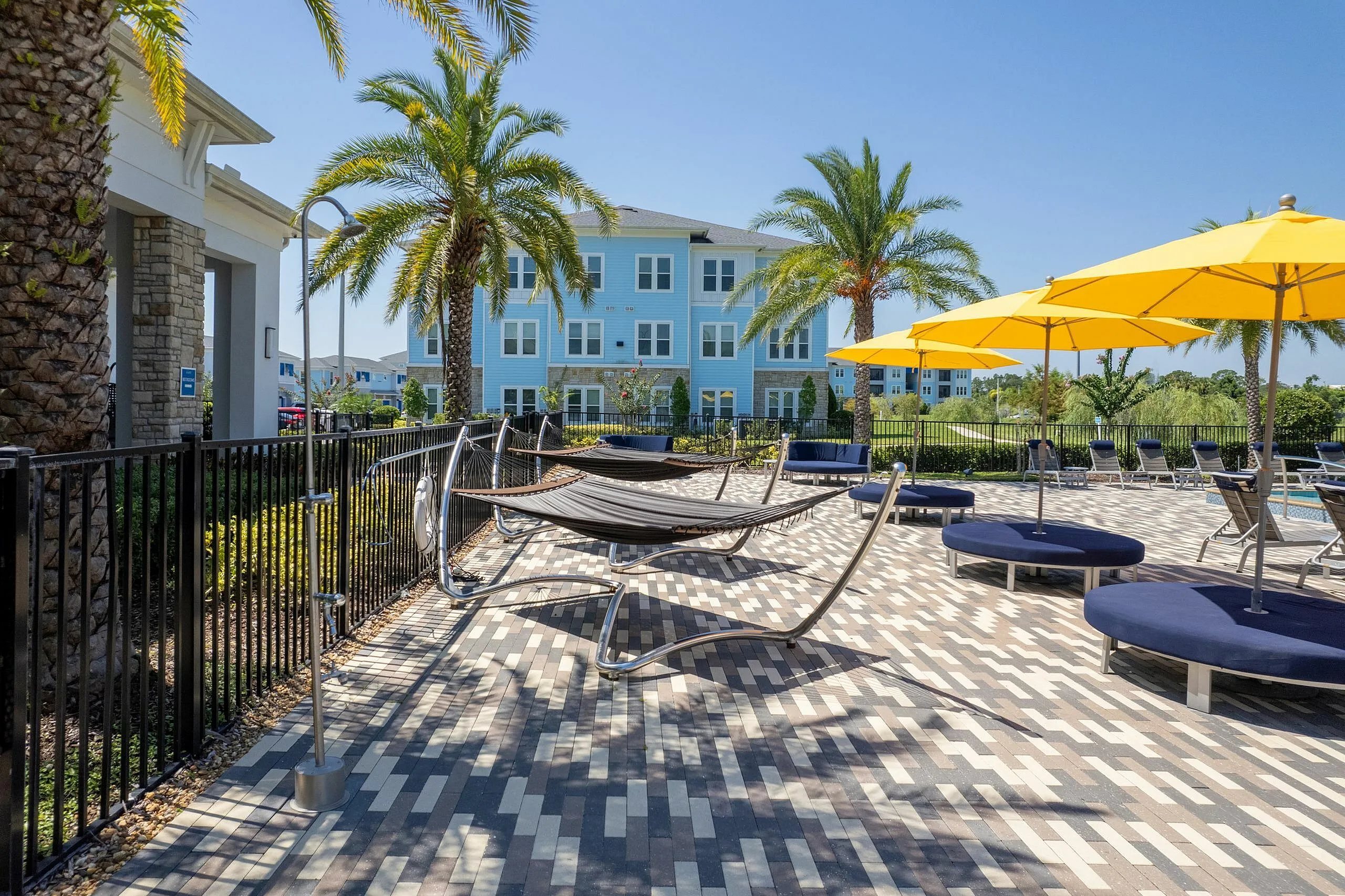 Serene apartment patio with cozy hammocks, vibrant yellow umbrellas, and lush palm trees.