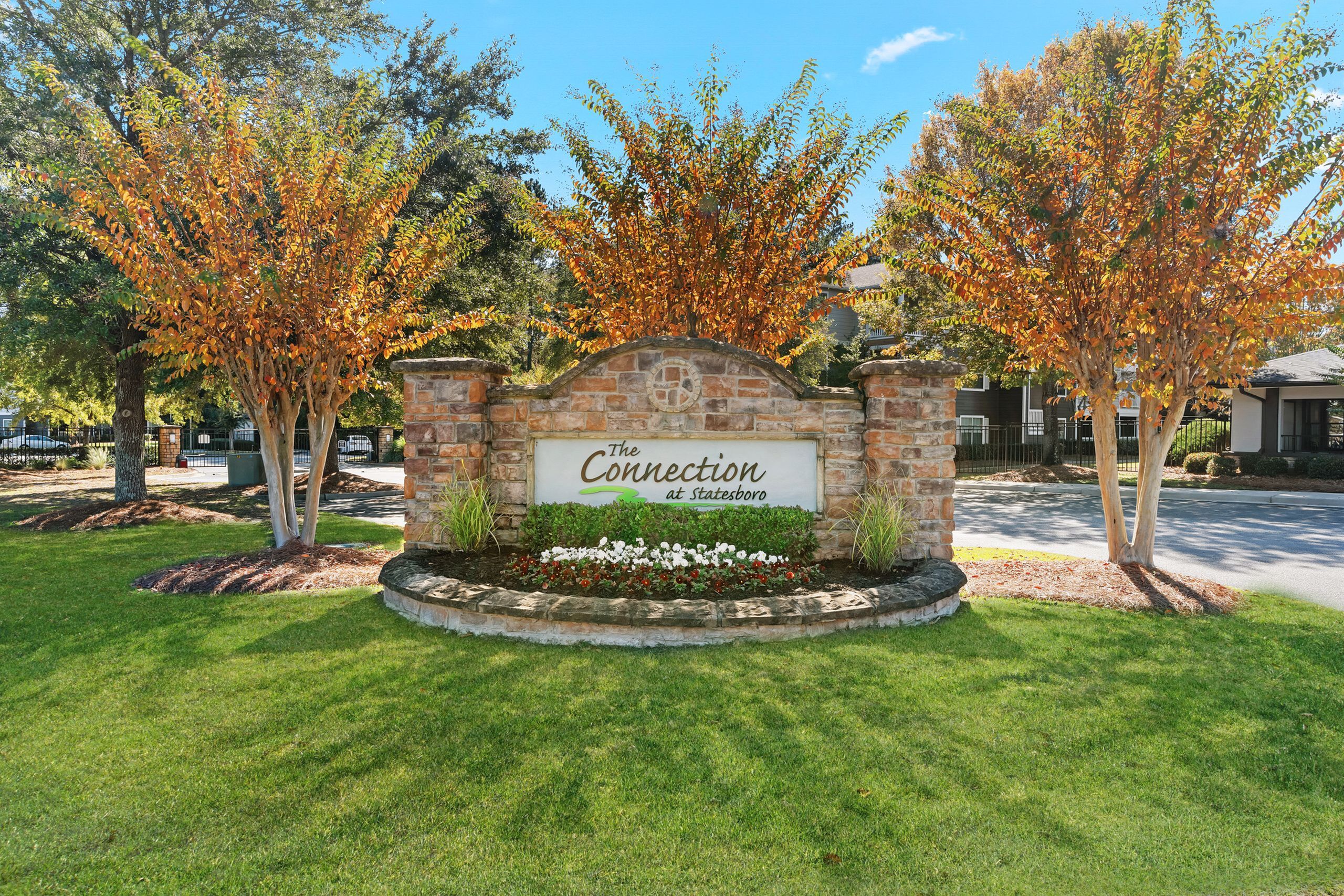 Inviting entrance of The Connection at Statesboro surrounded by lush green lawns and vibrant autumn trees.