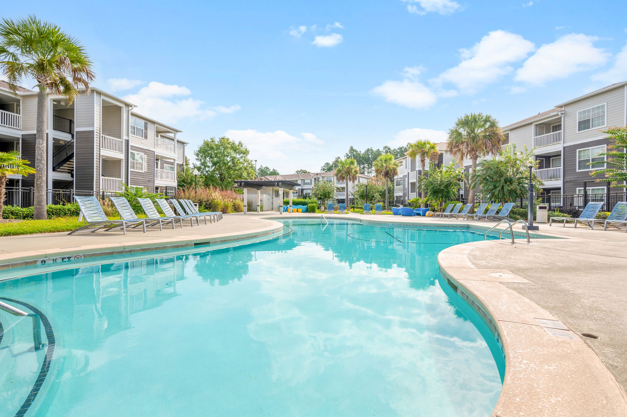 Luxury apartment complex with a pristine outdoor pool, surrounded by lush greenery and modern sun loungers, offering a serene retreat.