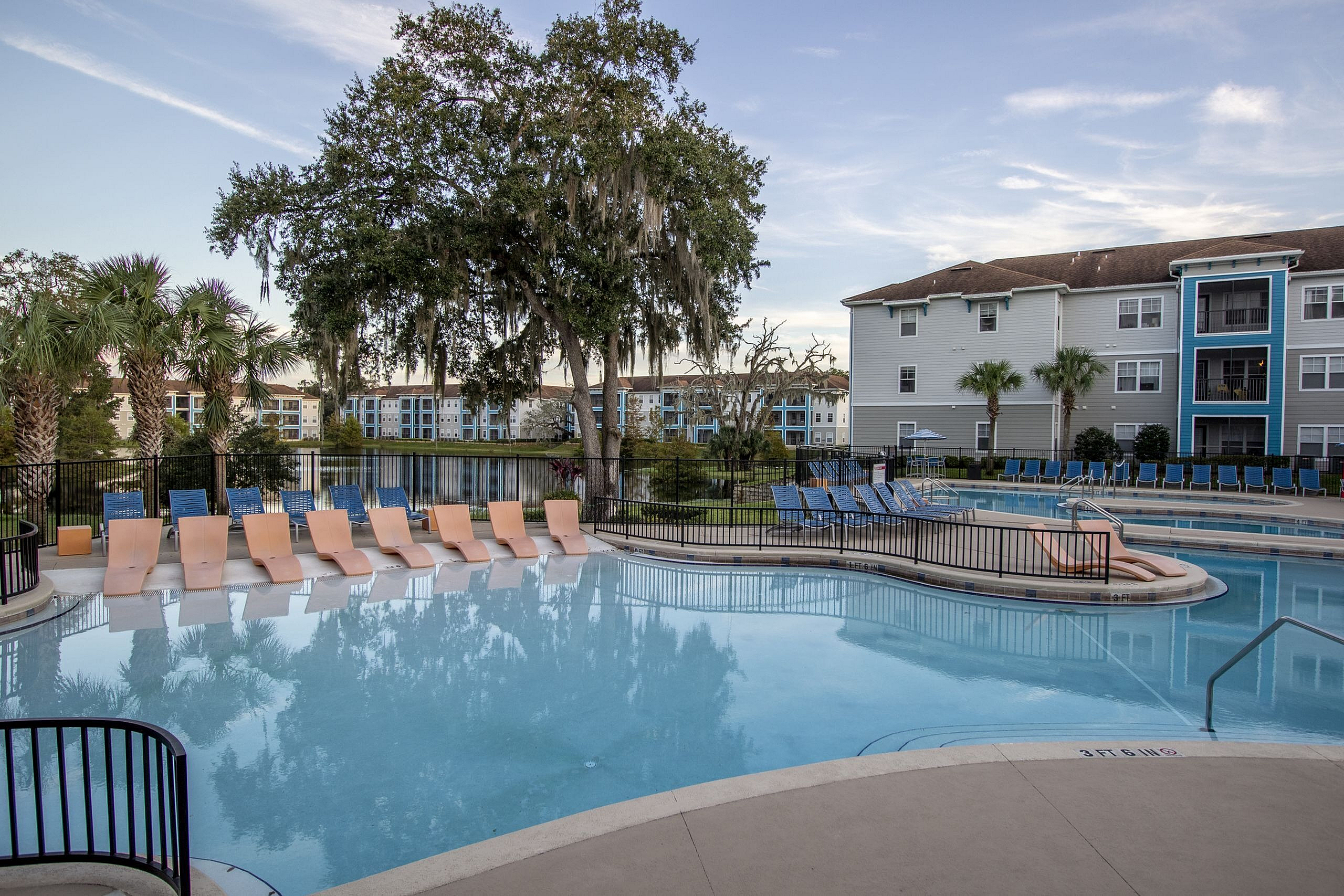 Inviting pool area with comfortable loungers, surrounded by lush greenery and modern apartments in the background, perfect for relaxation and leisure.