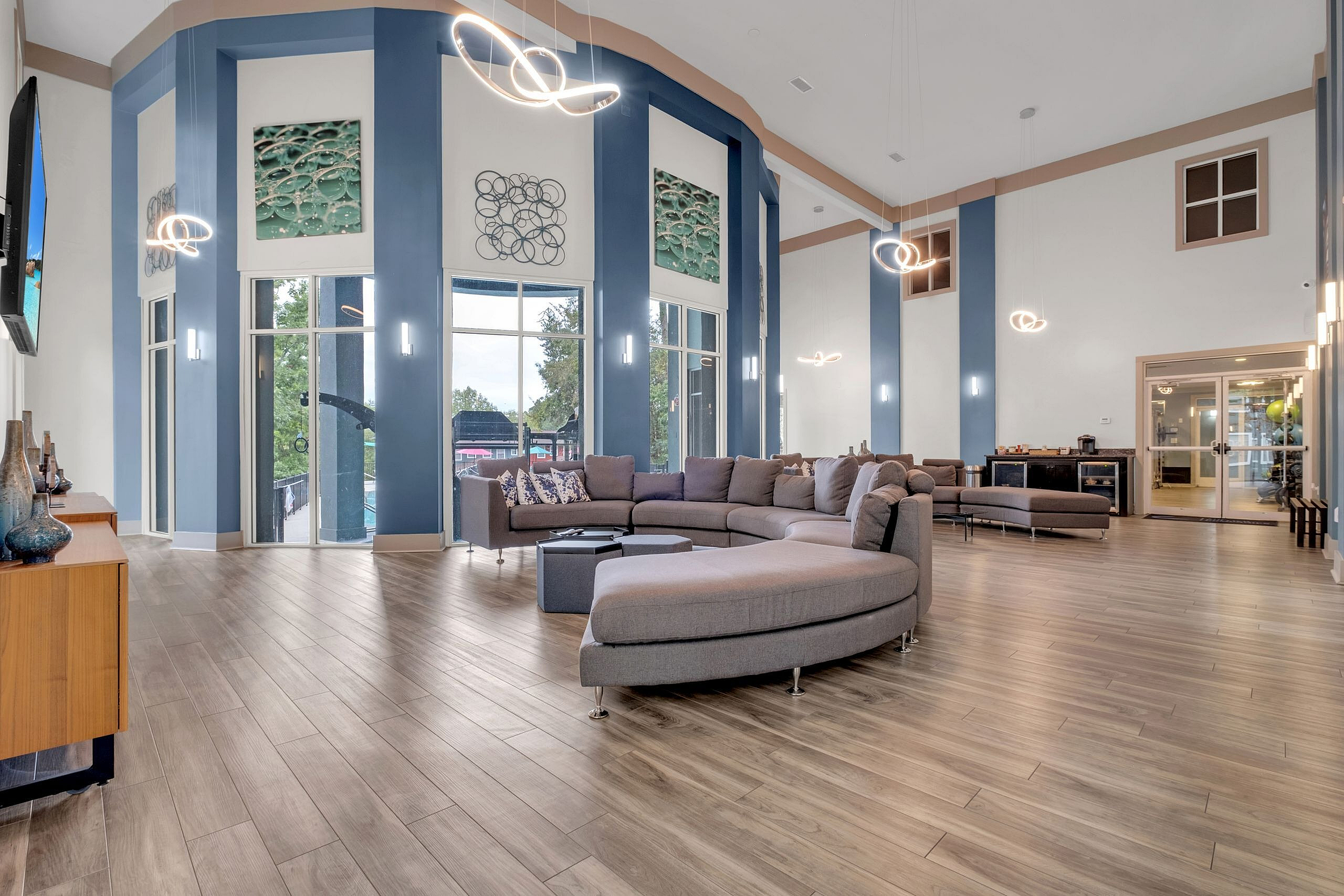 Elegant and modern communal lounge featuring chic circular sofas, high ceilings, large windows with garden views, and contemporary lighting.