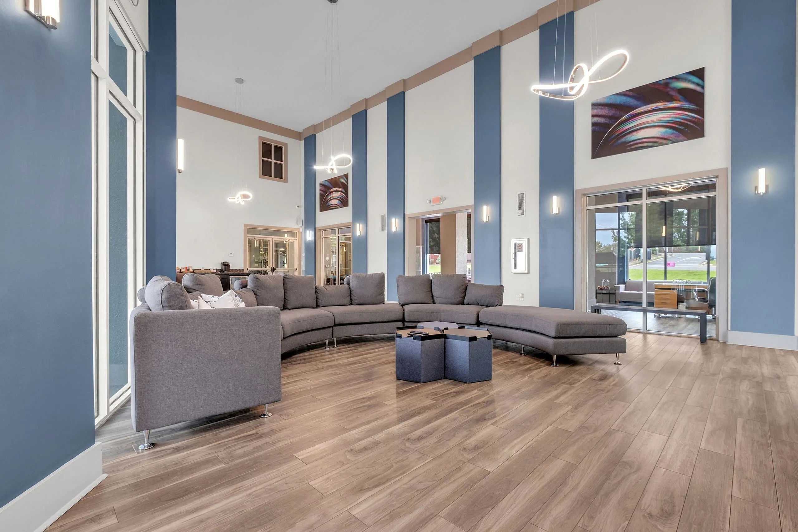 Elegant apartment lounge area featuring modern gray sectional sofas, sleek wood flooring, and stylish hanging light fixtures.