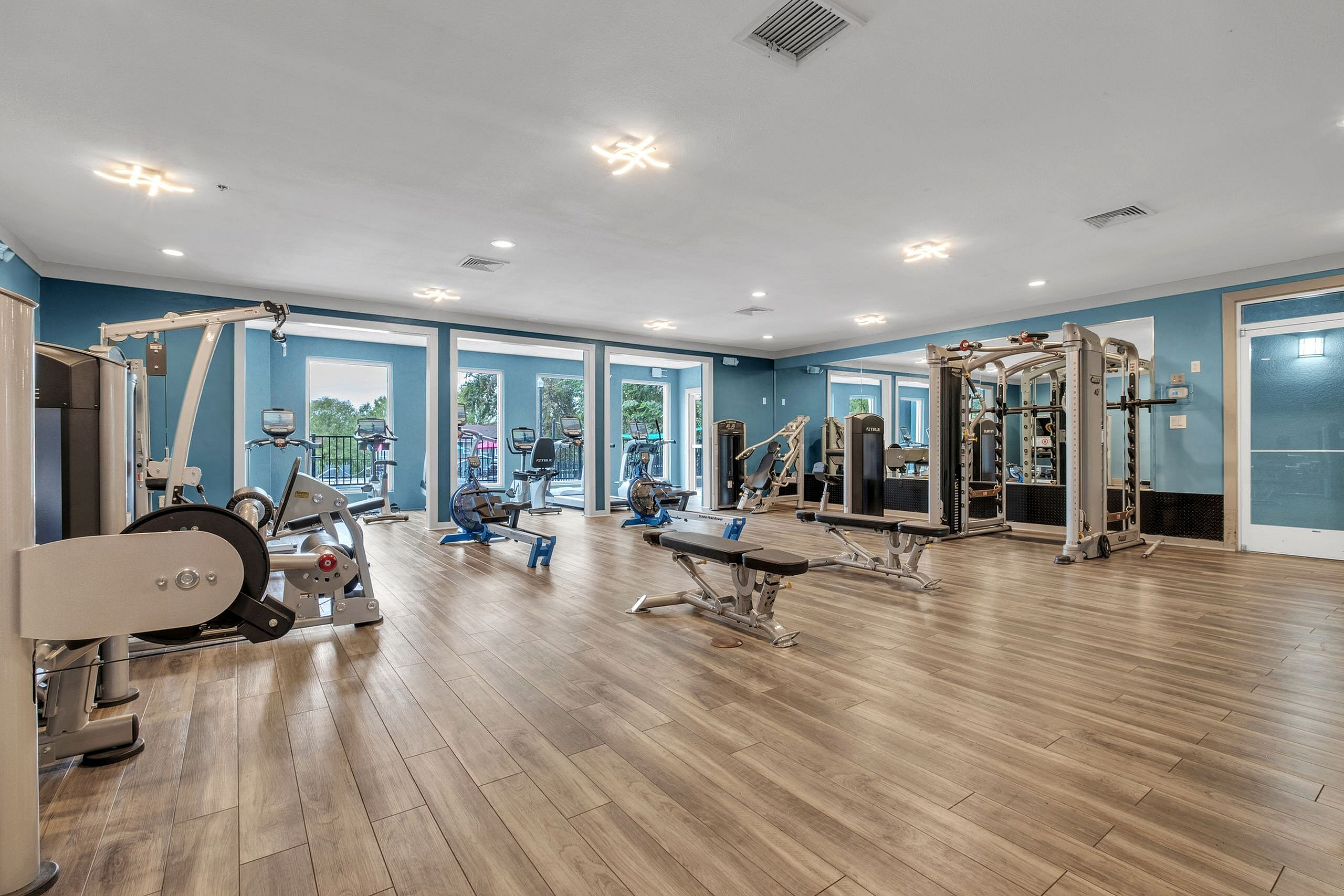 Bright and spacious fitness center with modern workout equipment, featuring large windows and sleek wooden flooring.