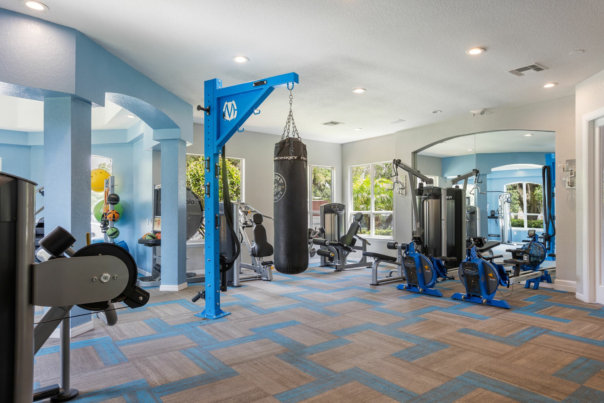 Modern fitness center with state-of-the-art equipment, vibrant blue accents, and natural light from large windows.