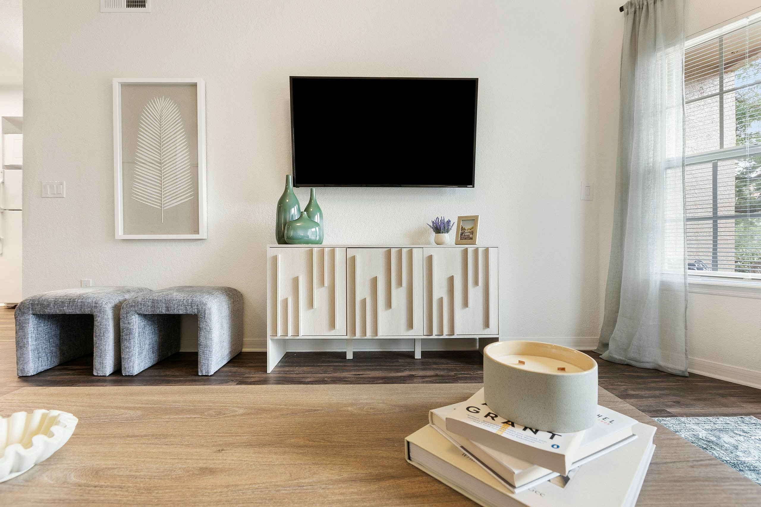 Bright and modern living room with elegant decor, featuring a stylish TV setup, minimalist artwork, and chic seating against a backdrop of natural light.