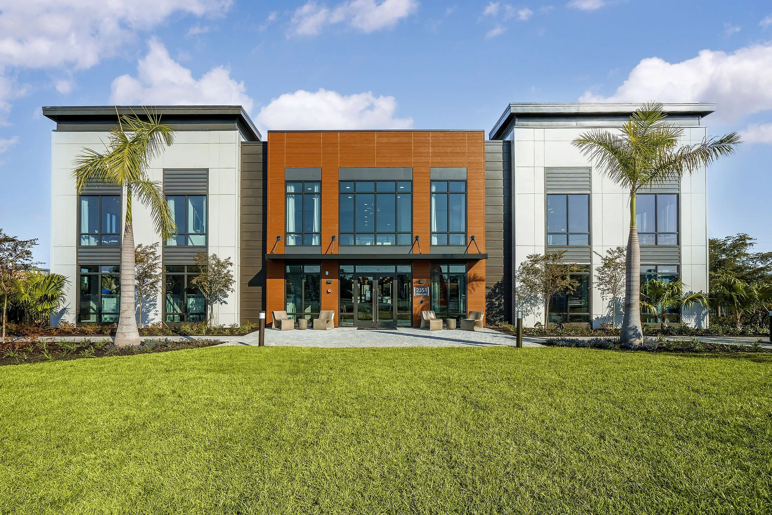 Modern apartment building with a sleek design, large windows, and lush green lawn accented by palm trees, promising luxury and style.