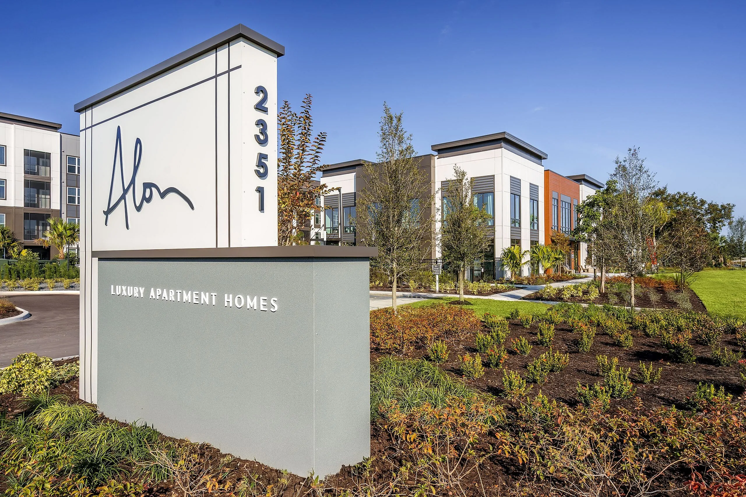 Modern luxury apartment complex featuring sleek architecture and beautifully landscaped gardens, highlighted by a prominent entrance sign with the address 2351.