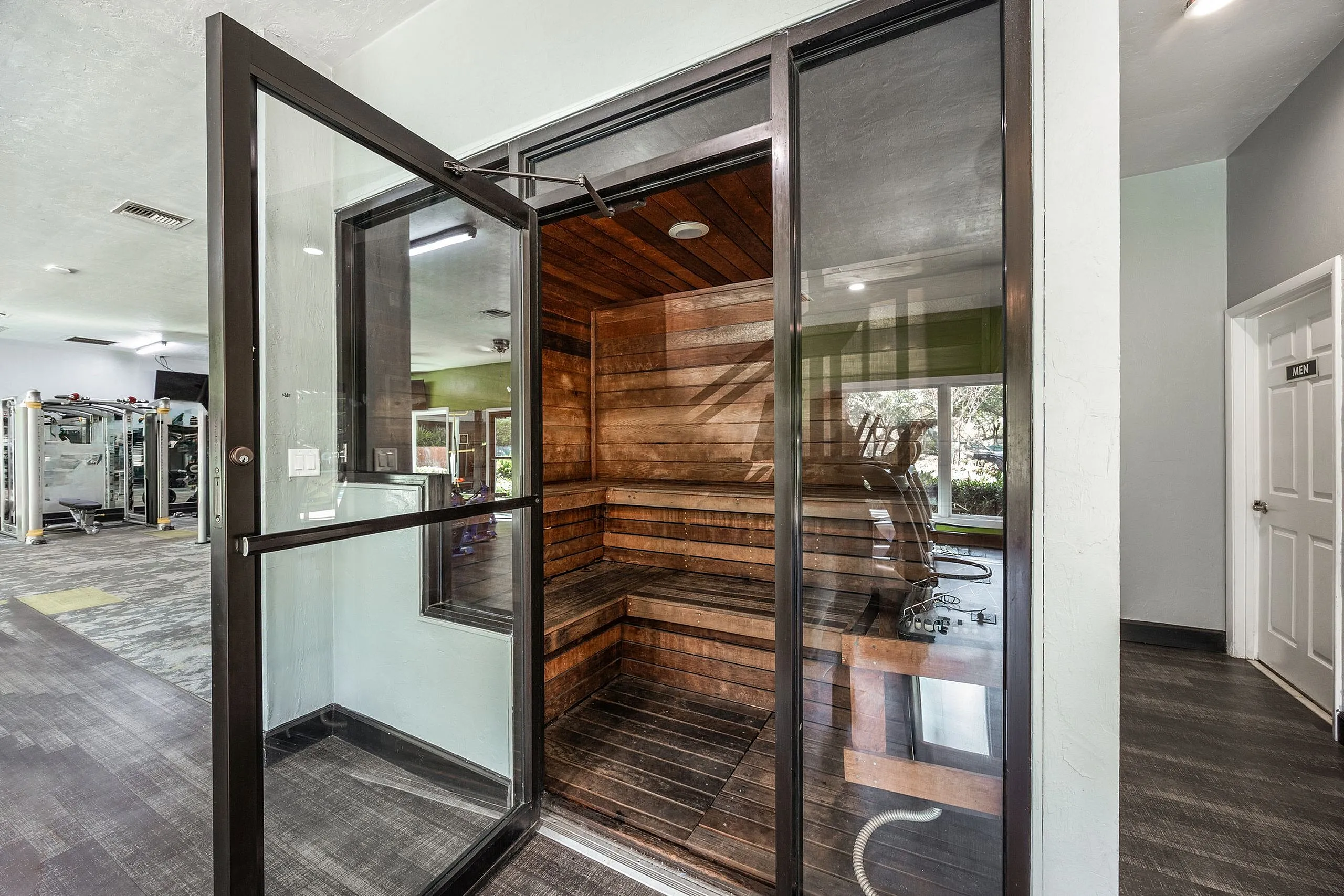 Modern gym facility featuring a luxurious wooden sauna with glass doors, offering a perfect retreat for relaxation and wellness.