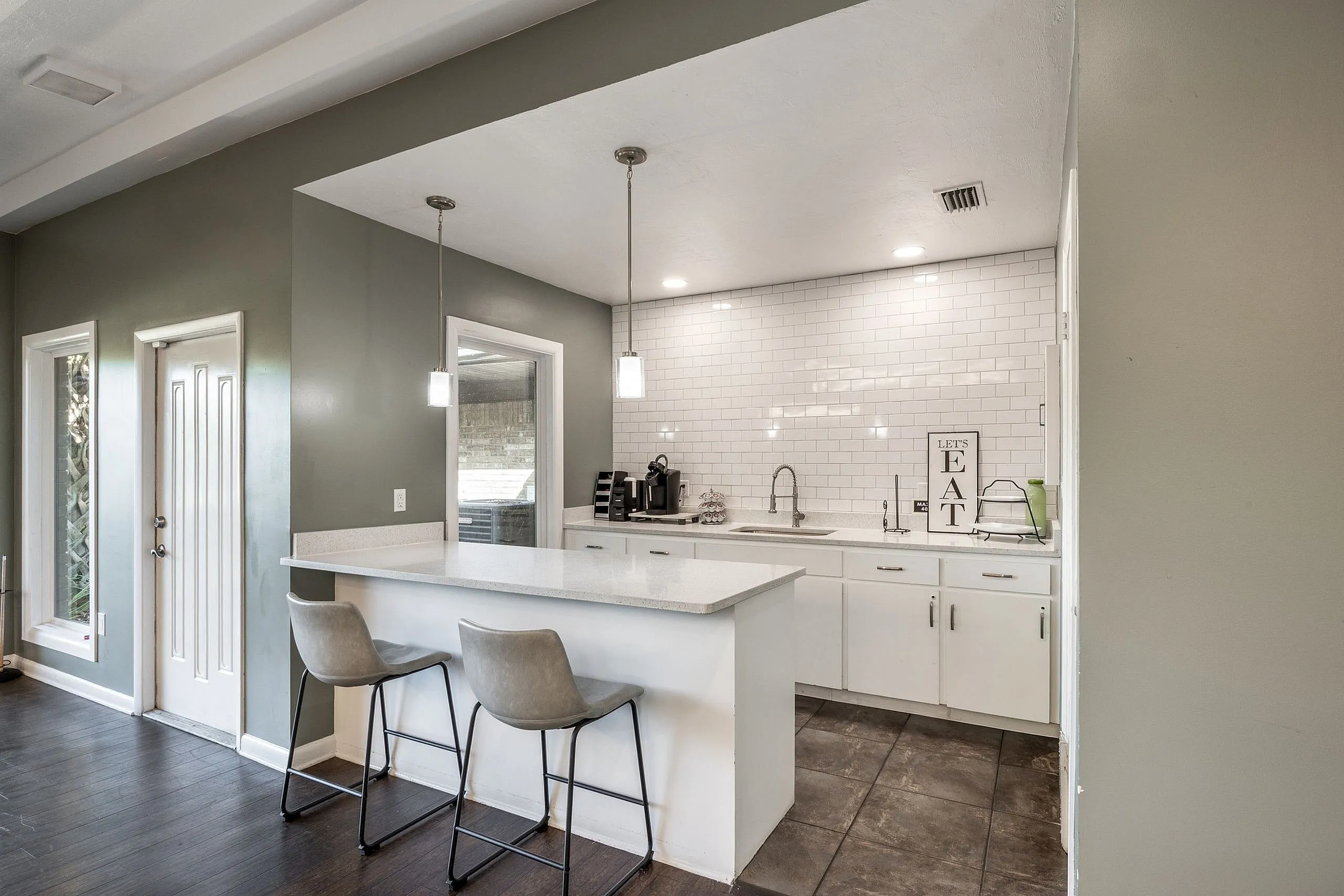 Modern kitchen with sleek white cabinetry, elegant pendant lighting, and a spacious breakfast bar with stylish seating, perfect for entertaining.