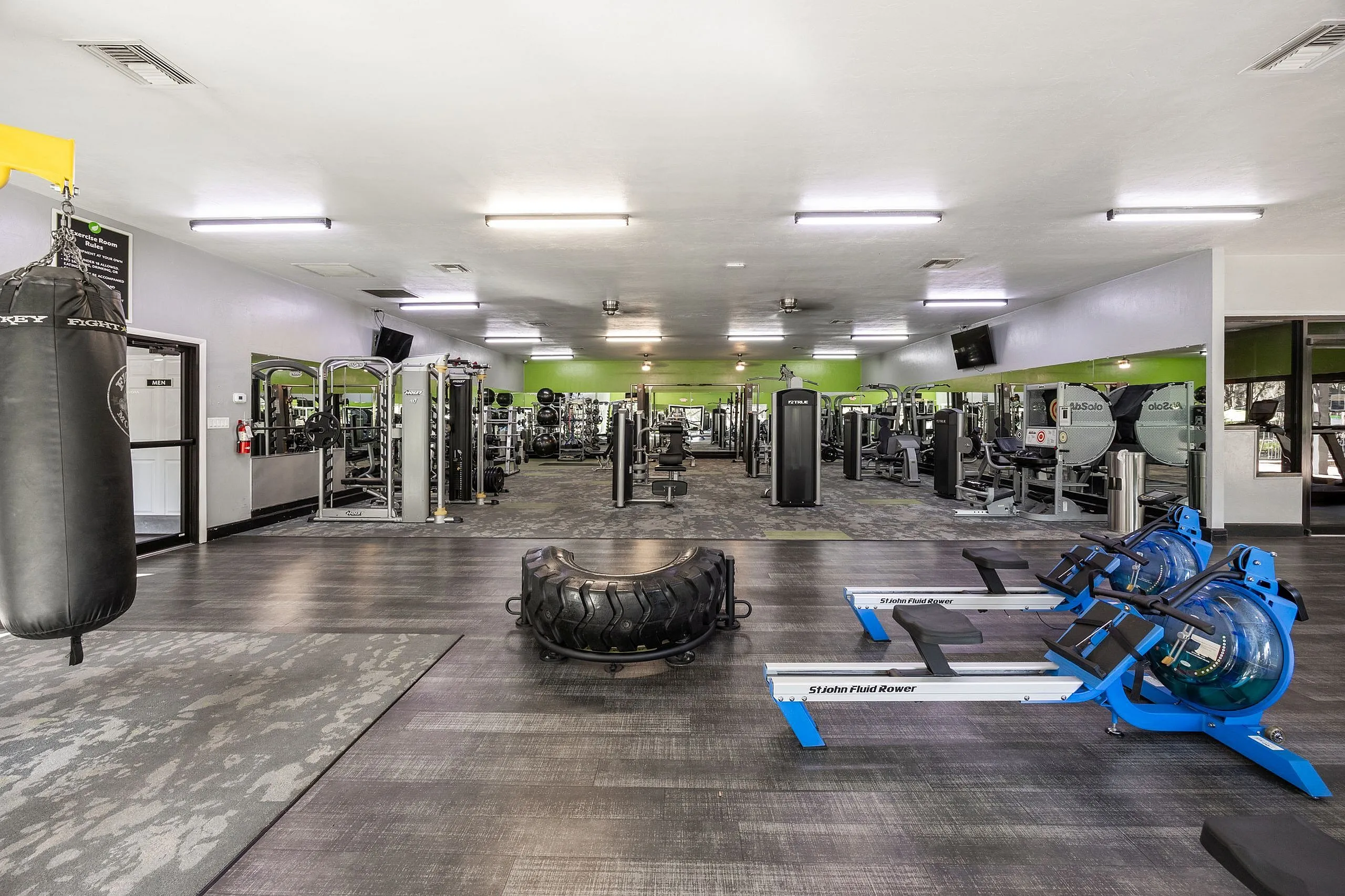 Spacious and modern apartment gym featuring state-of-the-art exercise equipment, sleek flooring, and bright green accents for an invigorating workout experience.