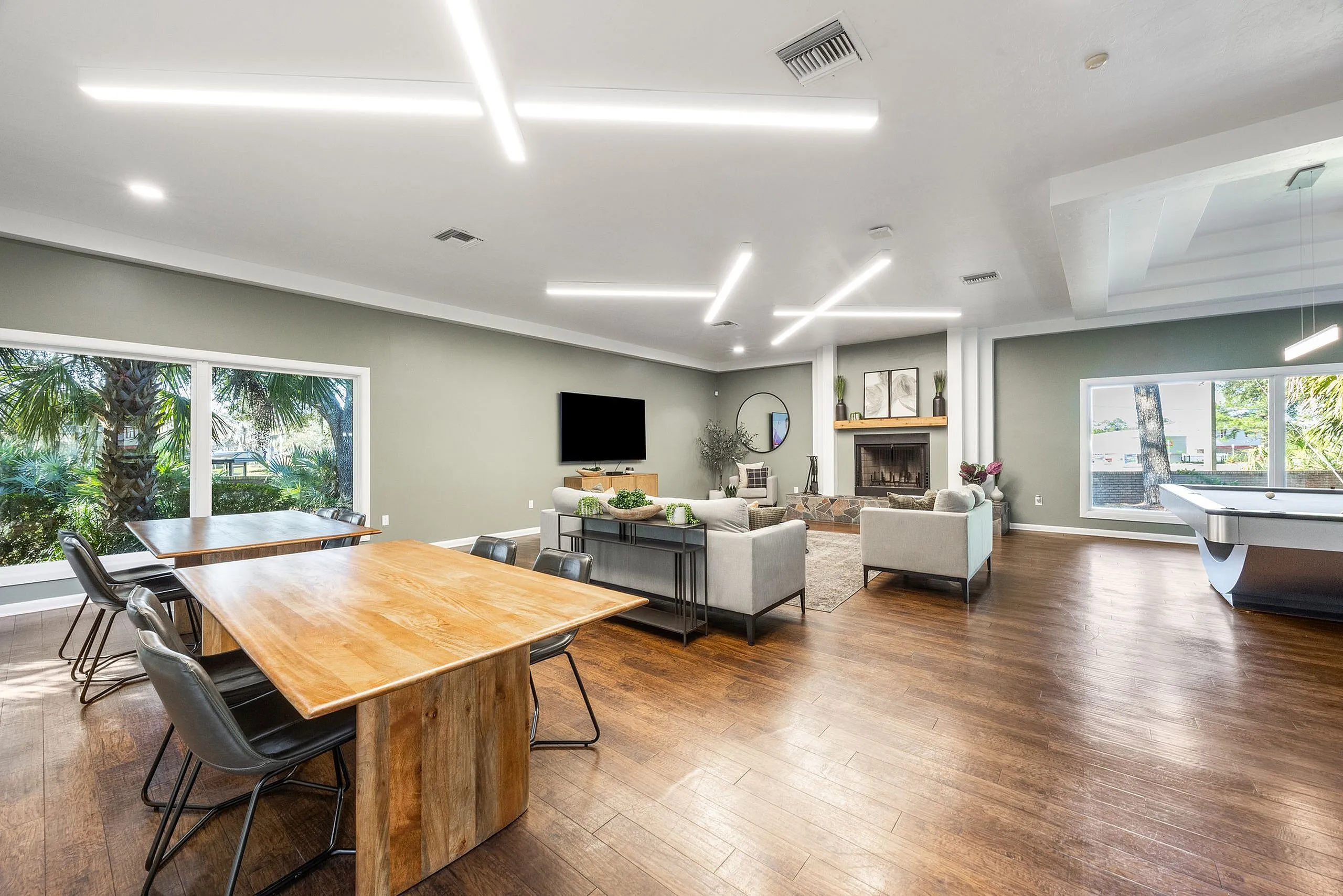 Spacious living area with modern seating, elegant wooden dining tables, and vibrant natural light from large windows, perfect for entertaining and relaxation.