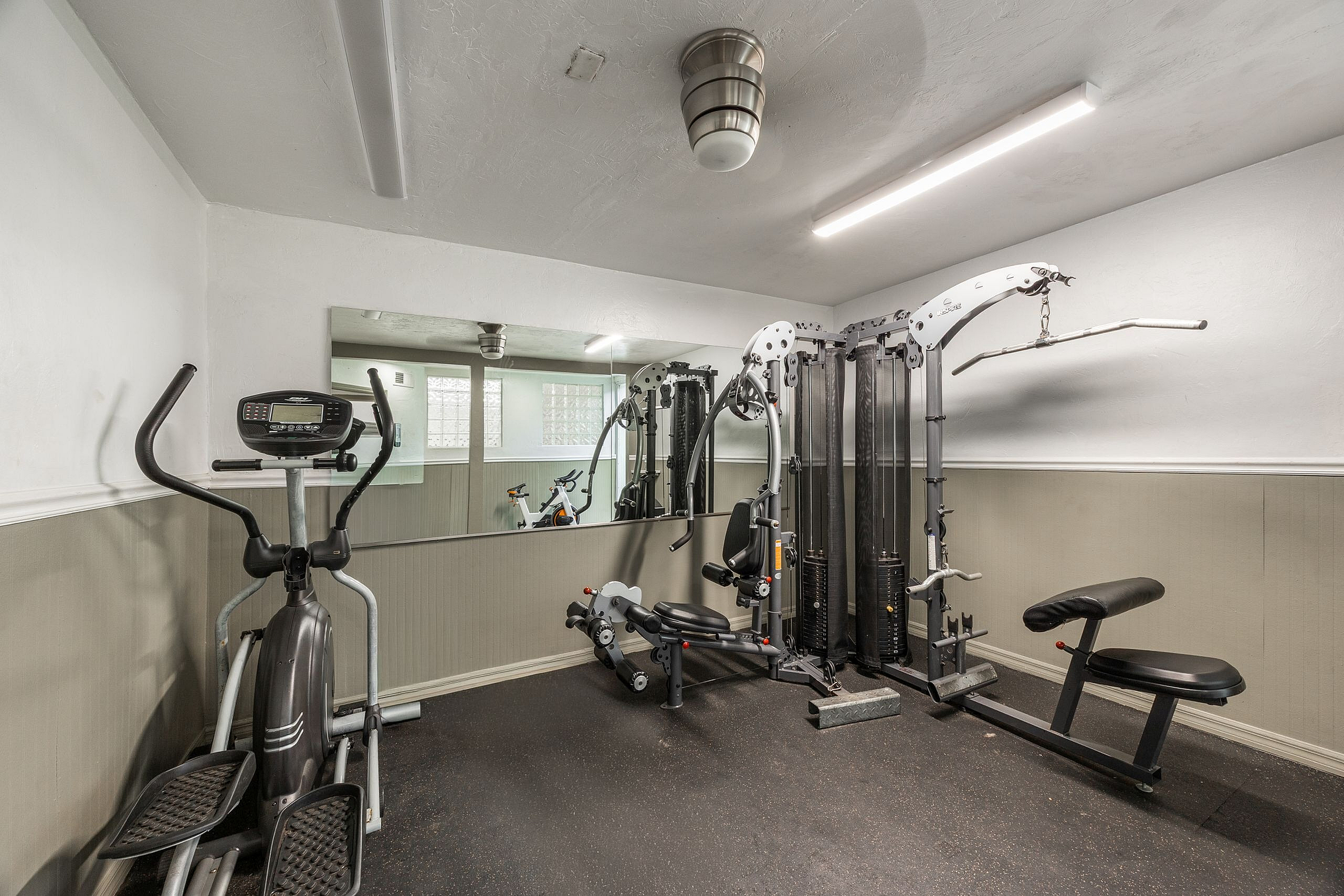 Modern apartment gym featuring high-quality fitness equipment, including an elliptical and weight machine in a well-lit space with mirrors.
