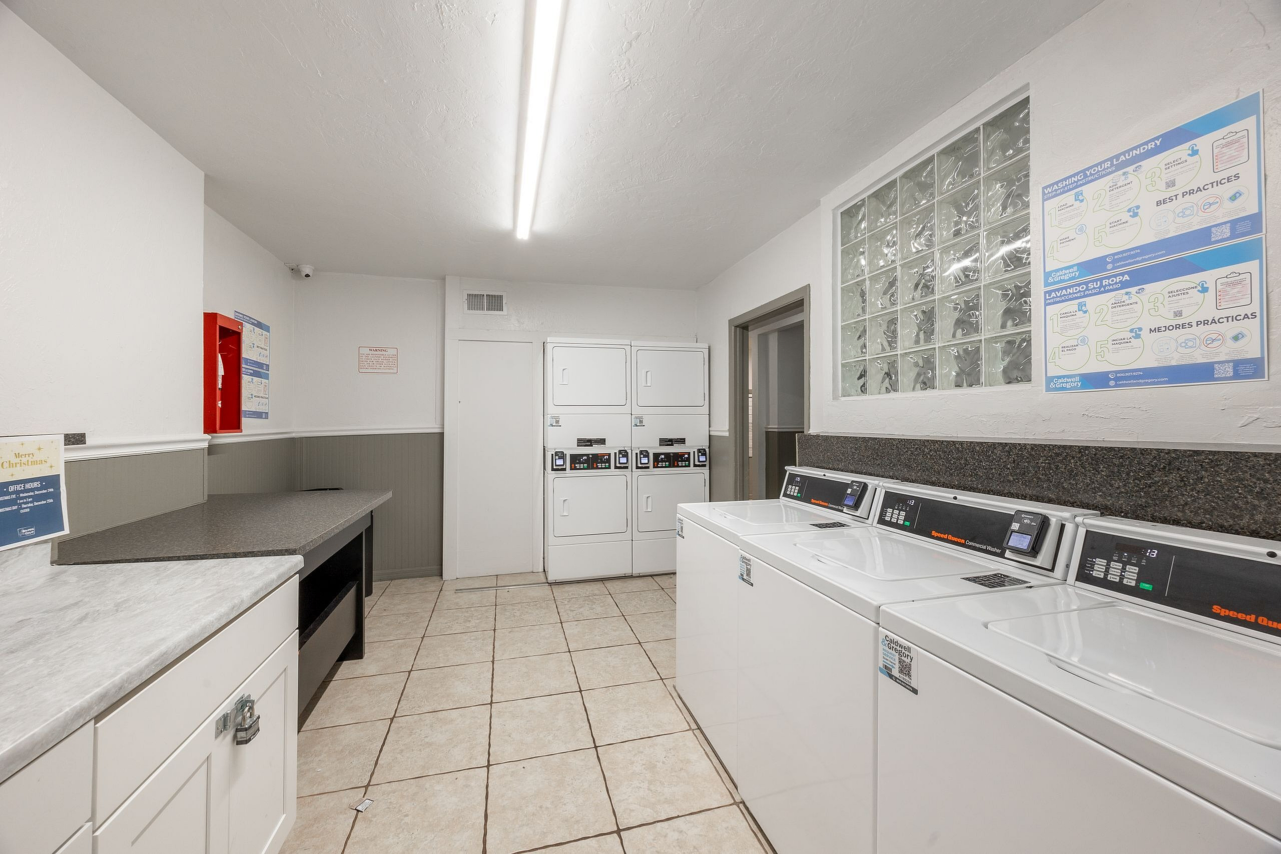 Bright and modern communal laundry room featuring high-efficiency washers and dryers, tiled flooring, and ample folding space.