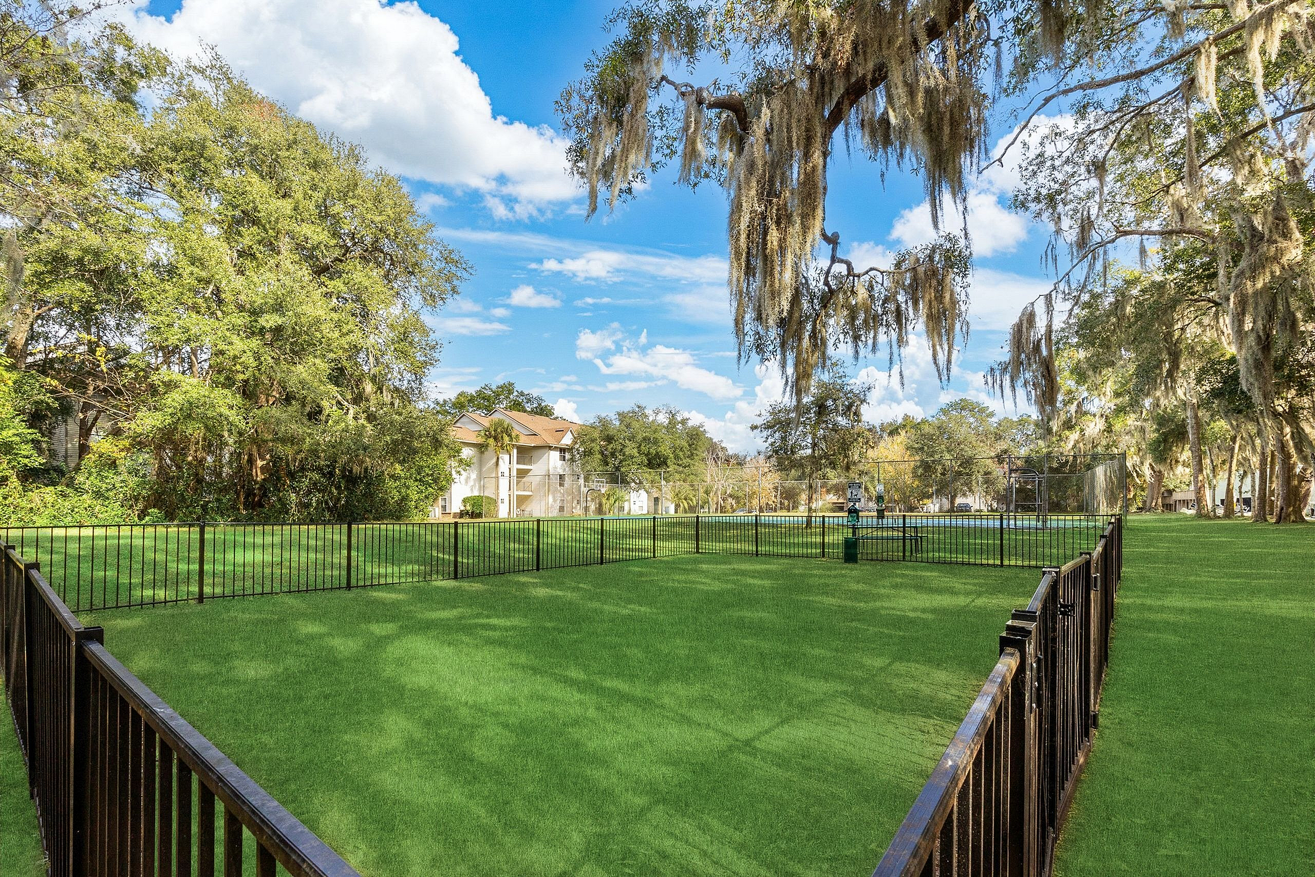 Charming outdoor space with lush green lawns, mature trees, and a cozy residential building in the background, ideal for relaxation and leisure.