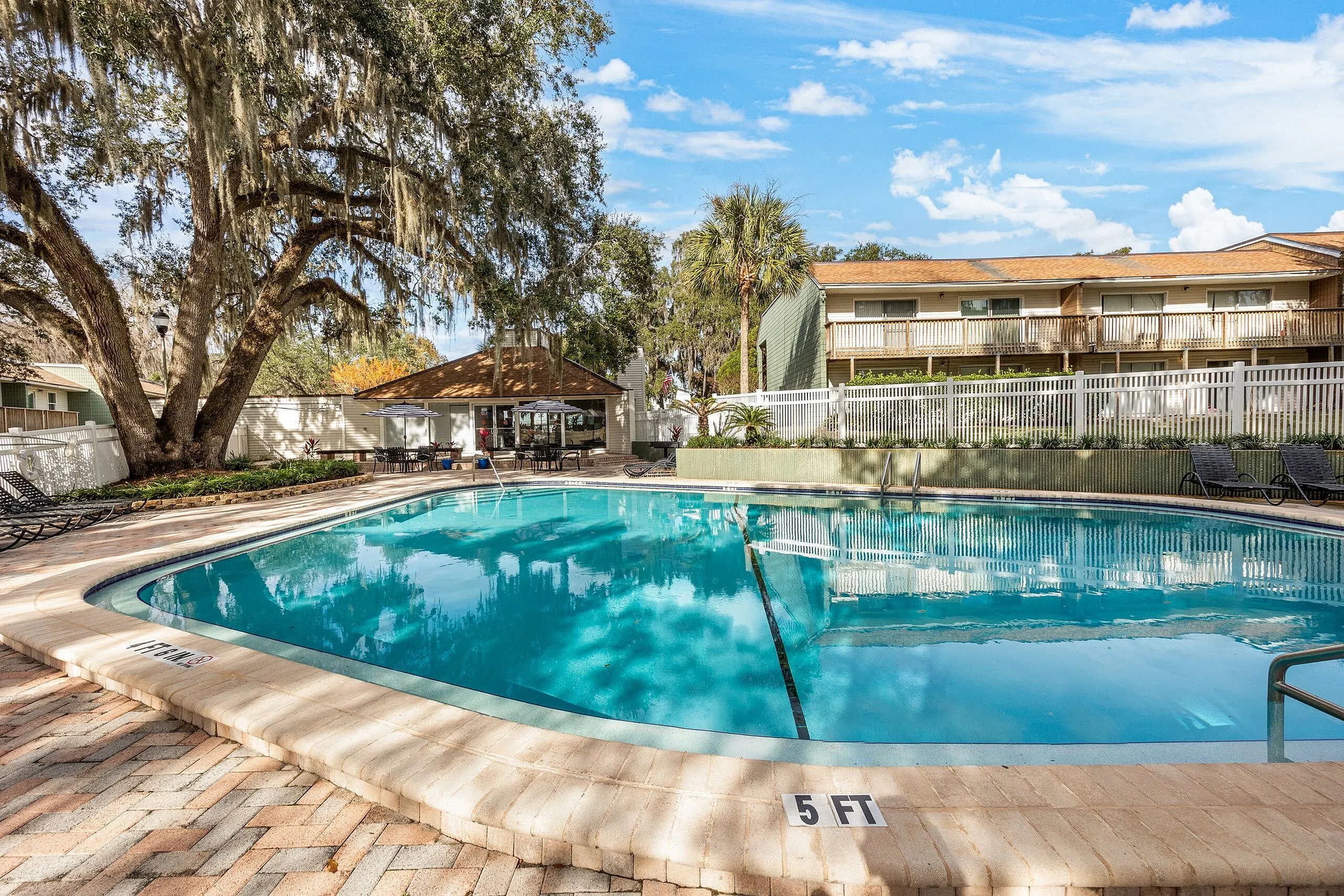 Inviting outdoor pool area surrounded by lush trees and modern apartments, perfect for relaxation and leisure under a bright blue sky.
