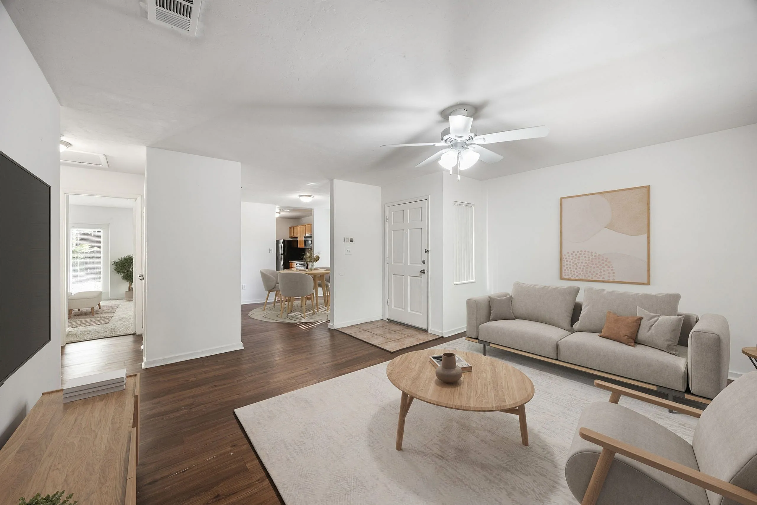 Bright and inviting living room with modern furniture, a cozy seating area, and sleek wooden flooring, leading to an open dining space and kitchen.