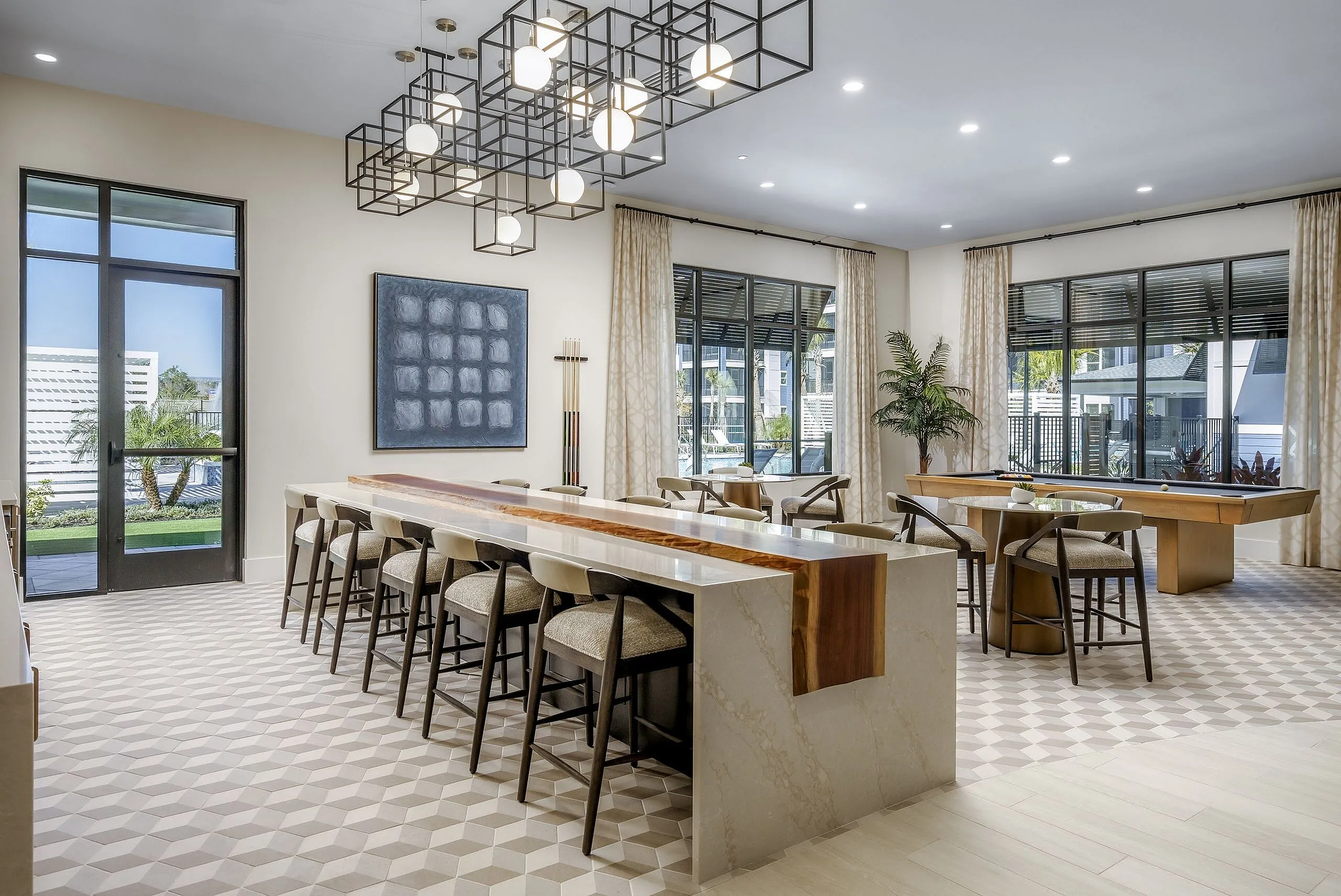 Elegant communal area featuring a stylish bar with high stools, impressive lighting fixtures, modern artwork, and large windows offering scenic views.