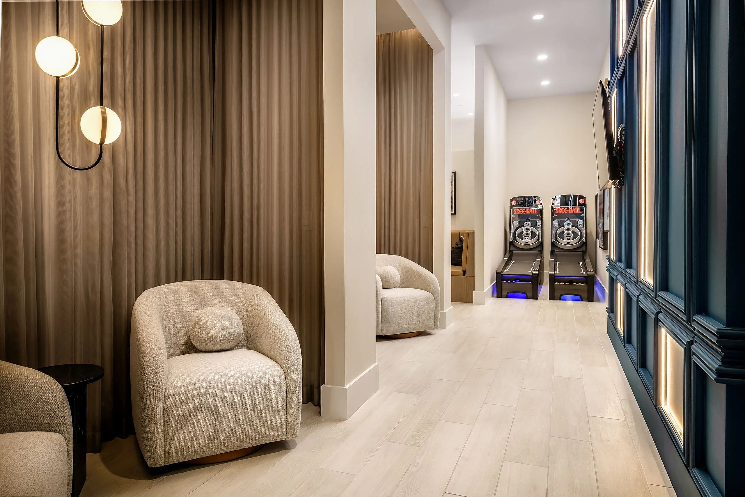 Luxurious lounge space with modern chairs, ambient lighting, and entertaining skee-ball games, highlighted by elegant wooden flooring and stylish decor.
