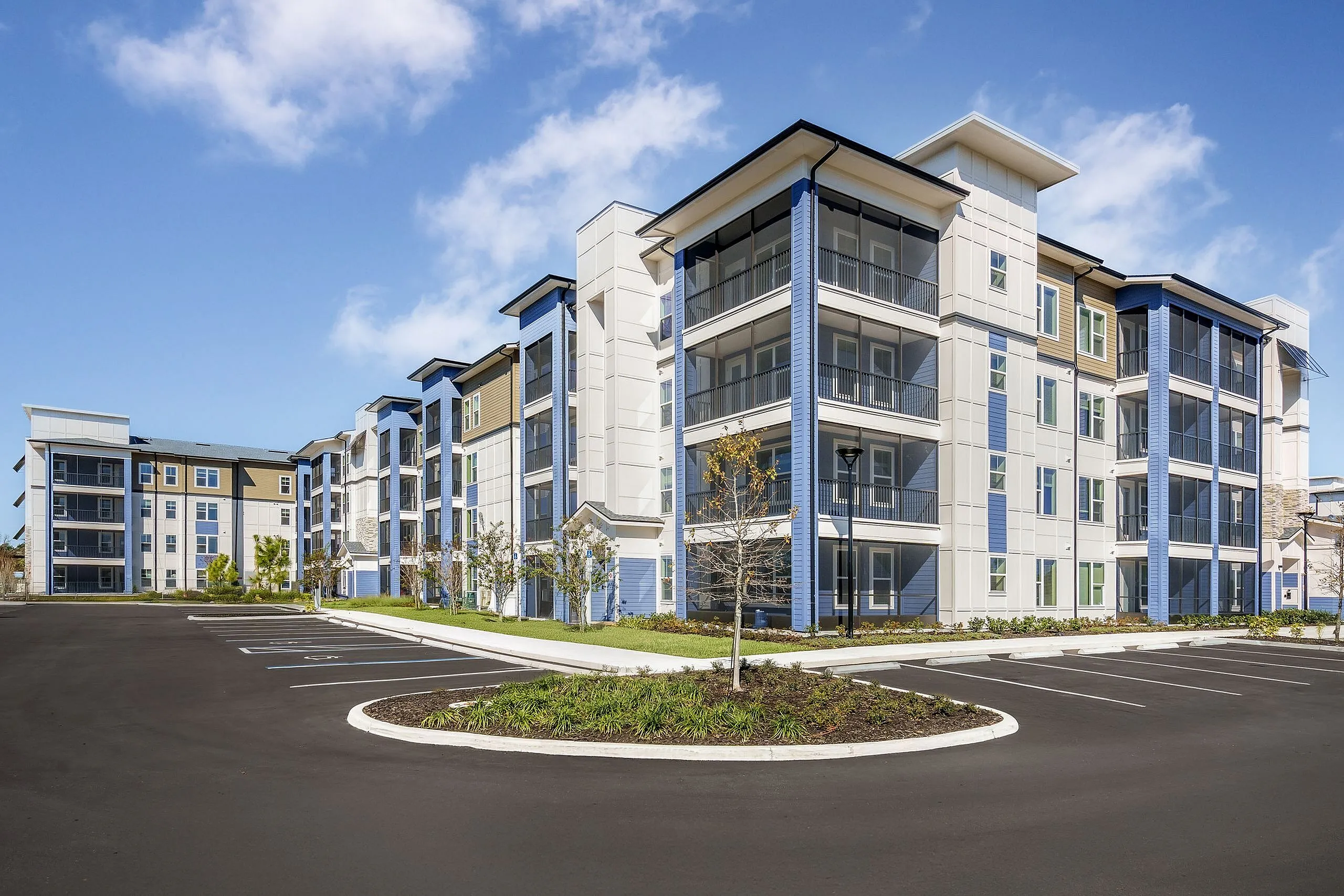 Modern apartment complex with sleek design, featuring spacious balconies and attractive architecture, set against a clear blue sky.