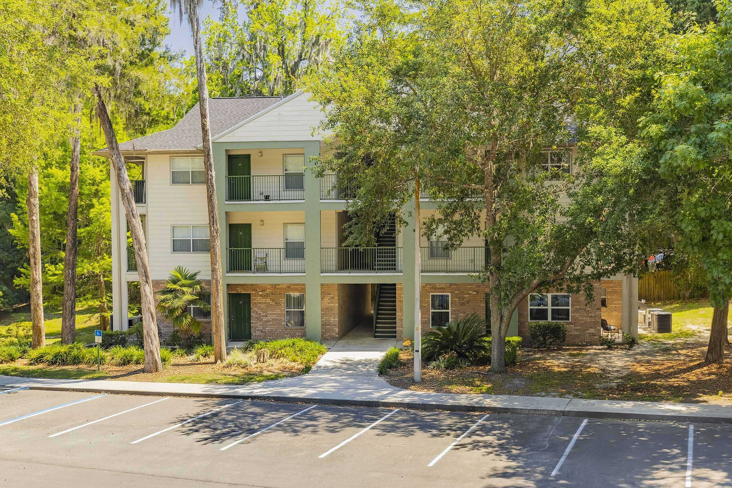 Charming three-story apartment building surrounded by lush greenery, featuring private balconies and ample parking space.