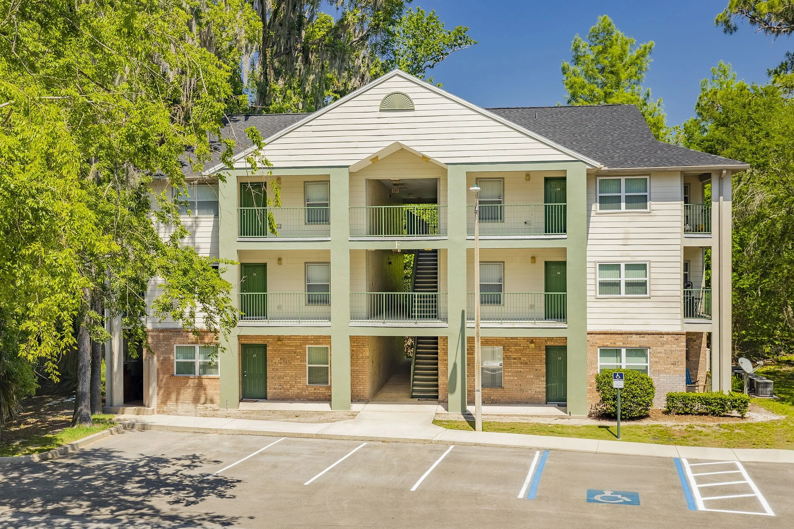 Charming three-story apartment building with green doors, surrounded by lush trees, providing serene living environment.