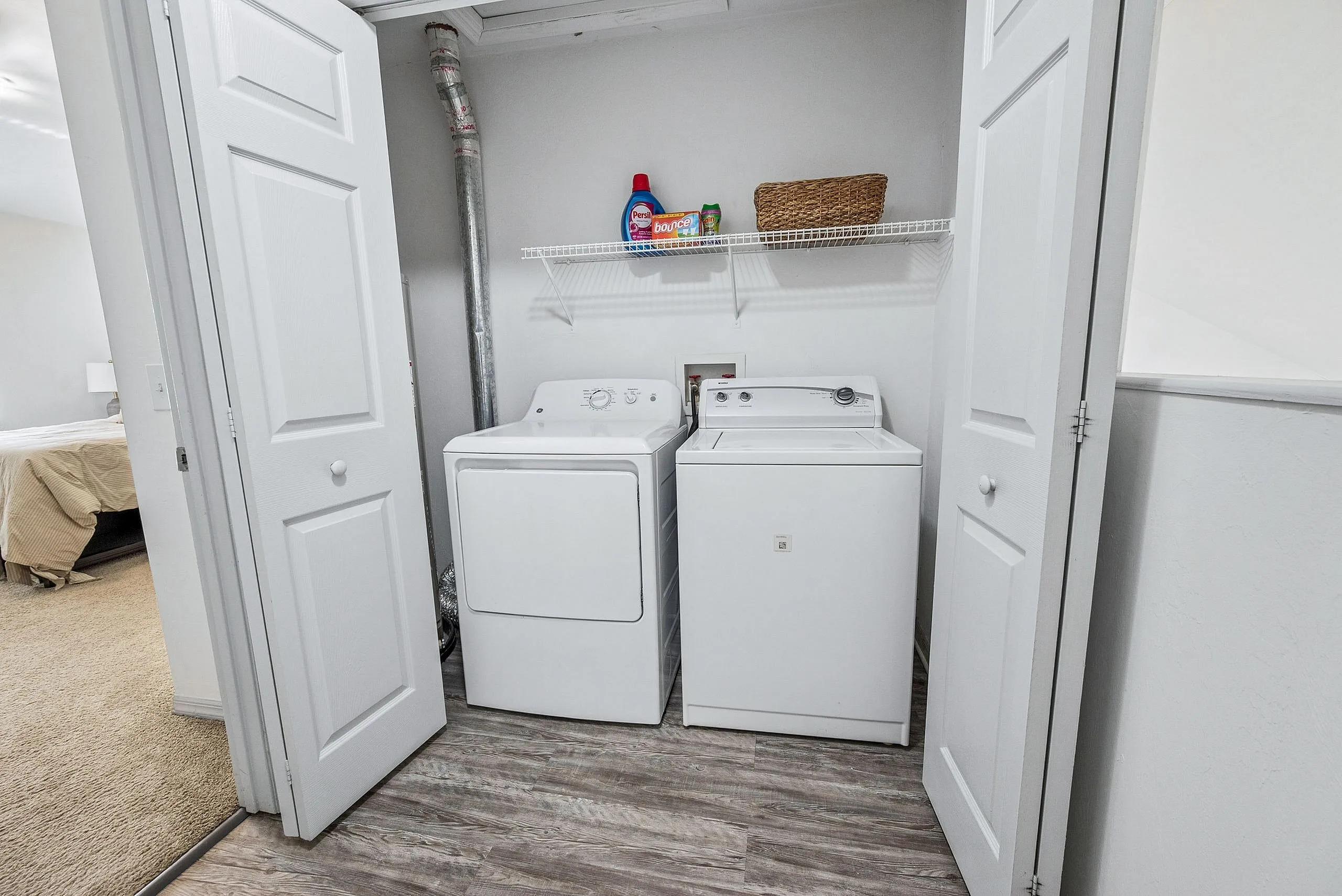 Charming laundry nook with modern washer and dryer, convenient shelving, and sleek flooring design.