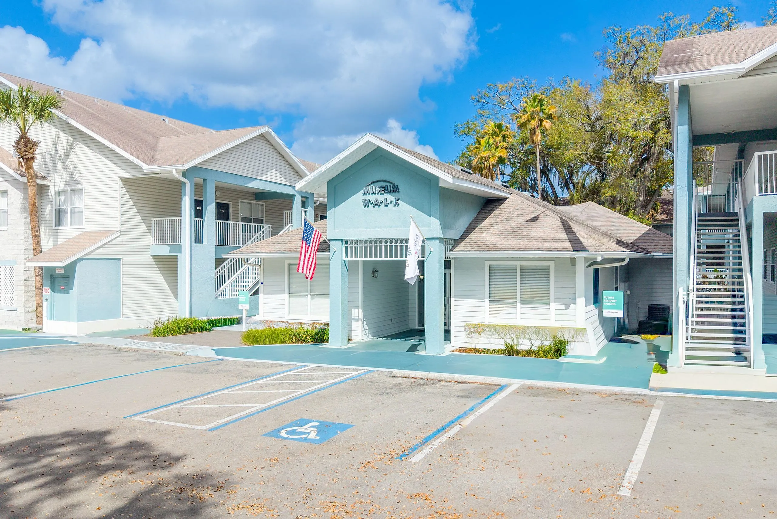 Charming apartment complex with inviting entrance, bright facade, and ample parking under a sunny sky.