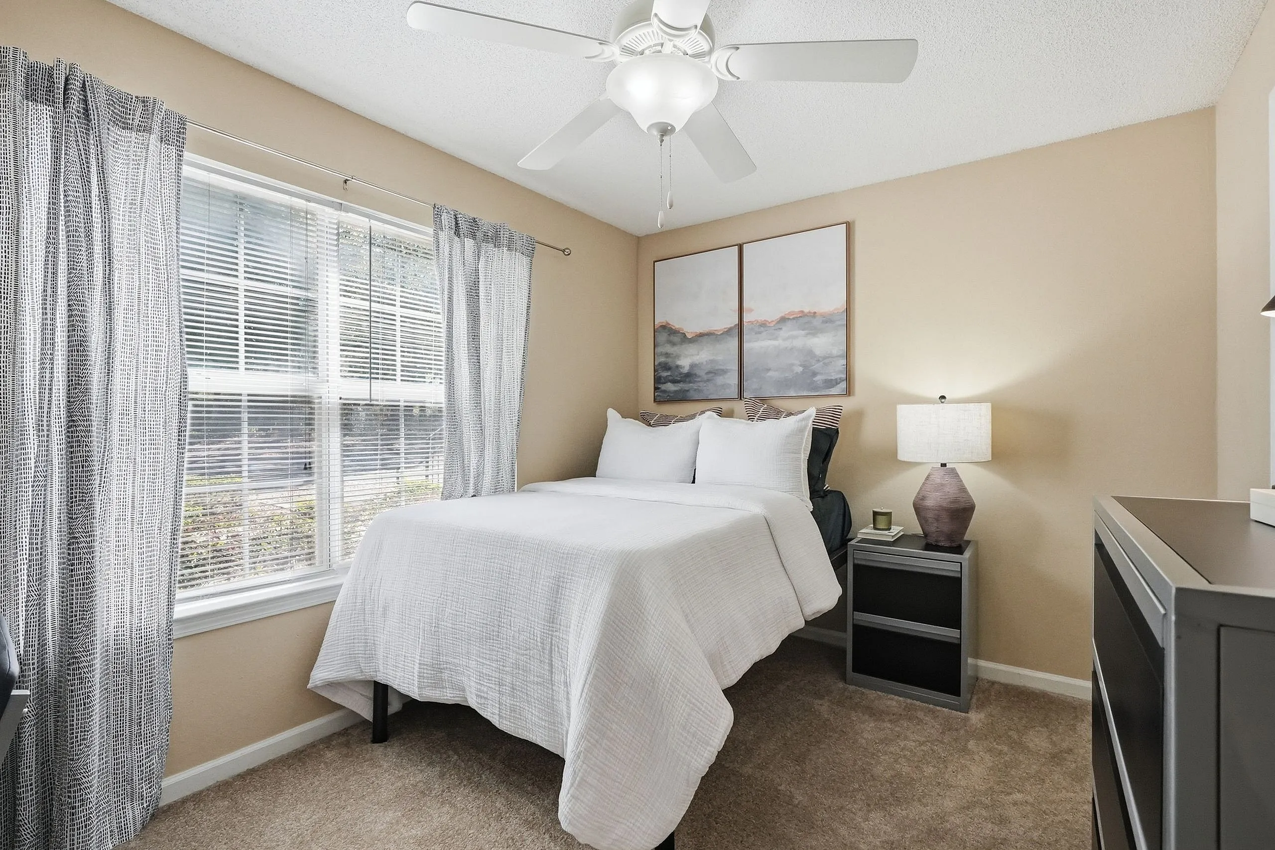 Cozy bedroom with soft lighting, elegant wall art, and a large window with patterned curtains, creating a bright, inviting atmosphere.