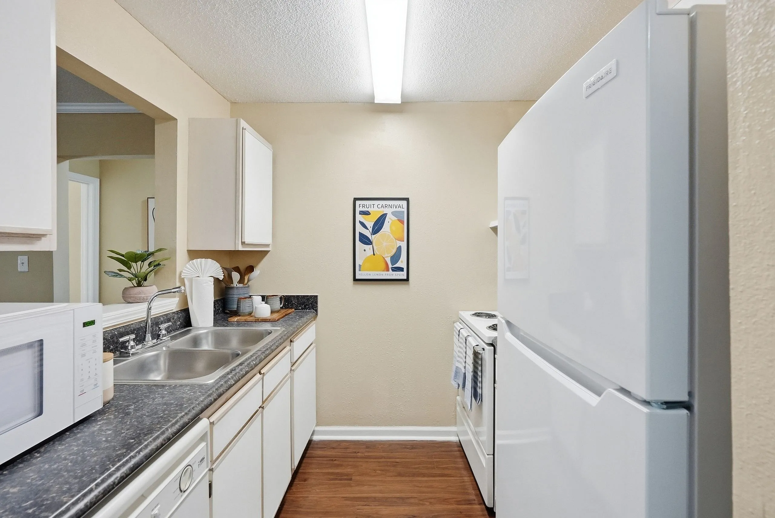 Modern and inviting kitchen with sleek appliances, double sink, and stylish countertop, highlighted by warm wood flooring and cheerful wall art.