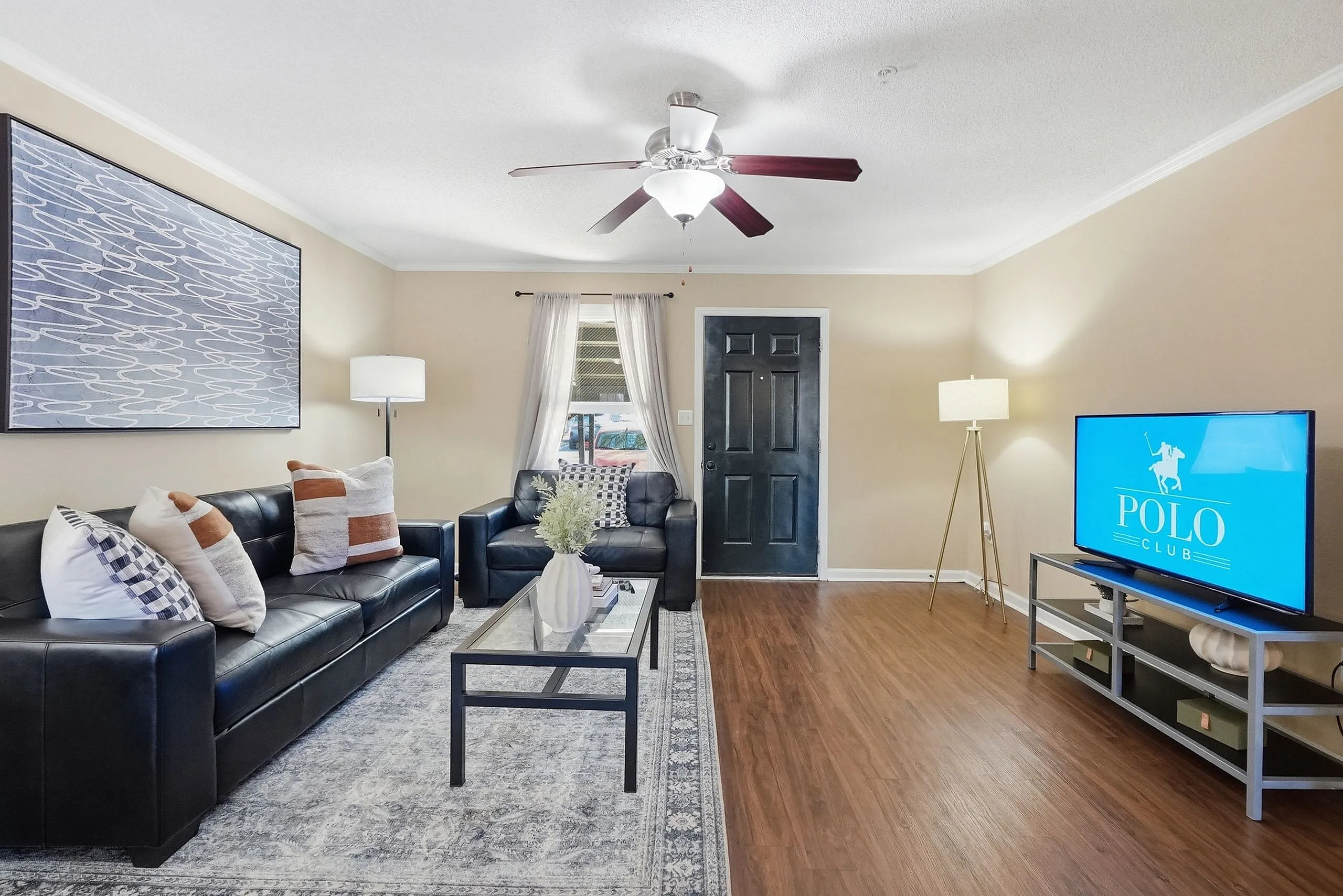 Inviting living room with sleek hardwood floors, black leather sofas, and stylish decor, ideal for relaxation and entertainment.