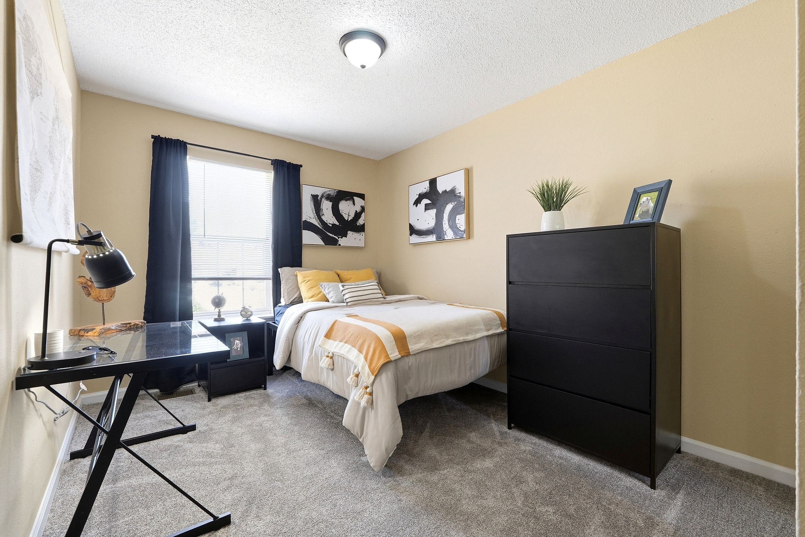 Inviting bedroom with cozy decor, featuring a comfortable bed, modern black dresser, and sleek workspace with ample natural light.