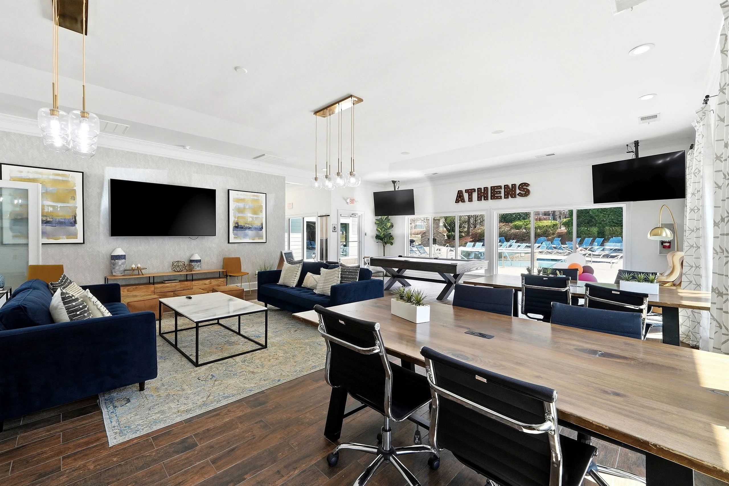 Luxurious community room with elegant seating, modern decor, and large windows overlooking a vibrant outdoor pool.