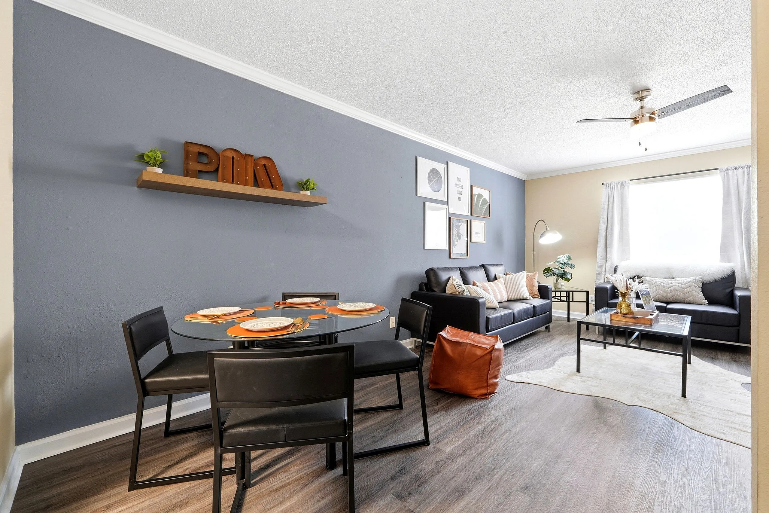 Modern open-concept living and dining area with stylish décor, featuring a sleek glass dining table, cozy leather sofa, and contemporary artwork.
