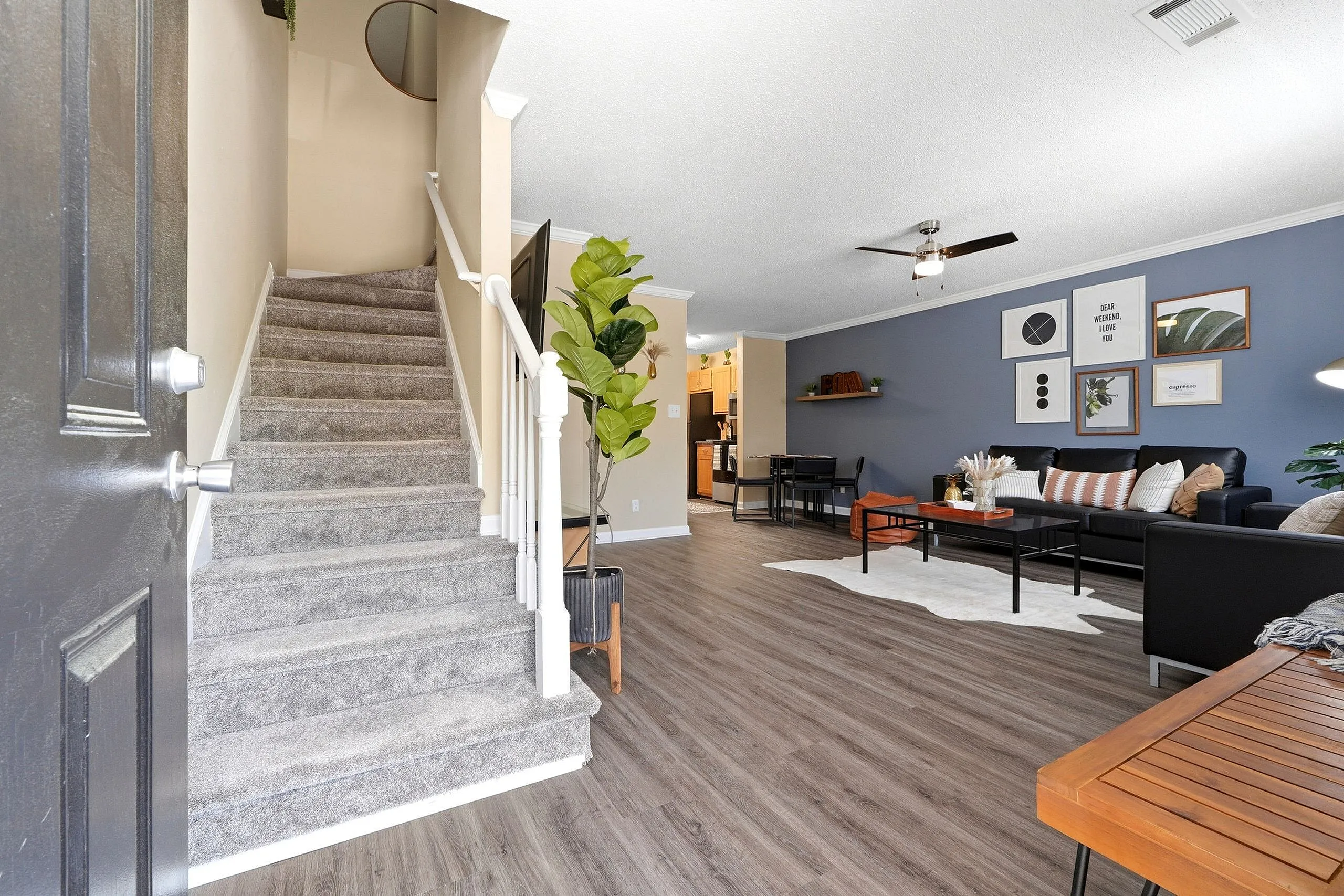 Modern open-plan living space with stylish decor, featuring a cozy lounge area with artful wall designs, contemporary dining setting, and plush carpeted staircase.