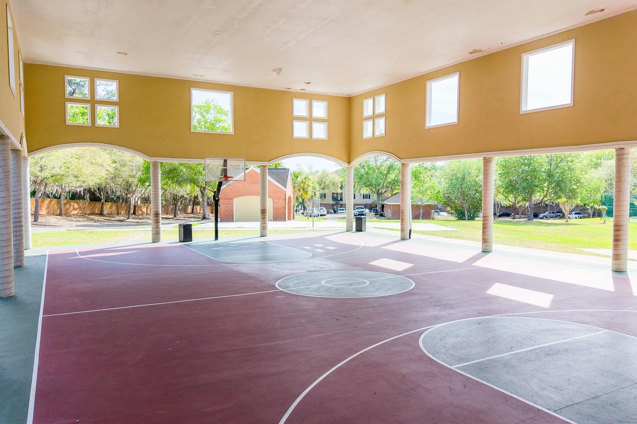 Spacious indoor basketball court with sunlit open walls and a view of lush greenery.