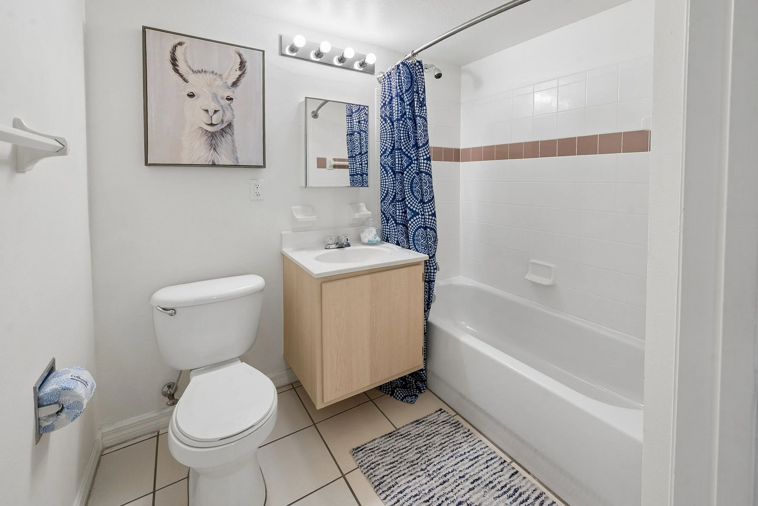 Bright and modern bathroom featuring a stylish llama artwork, elegant vanity, and cozy bathtub with a patterned shower curtain.