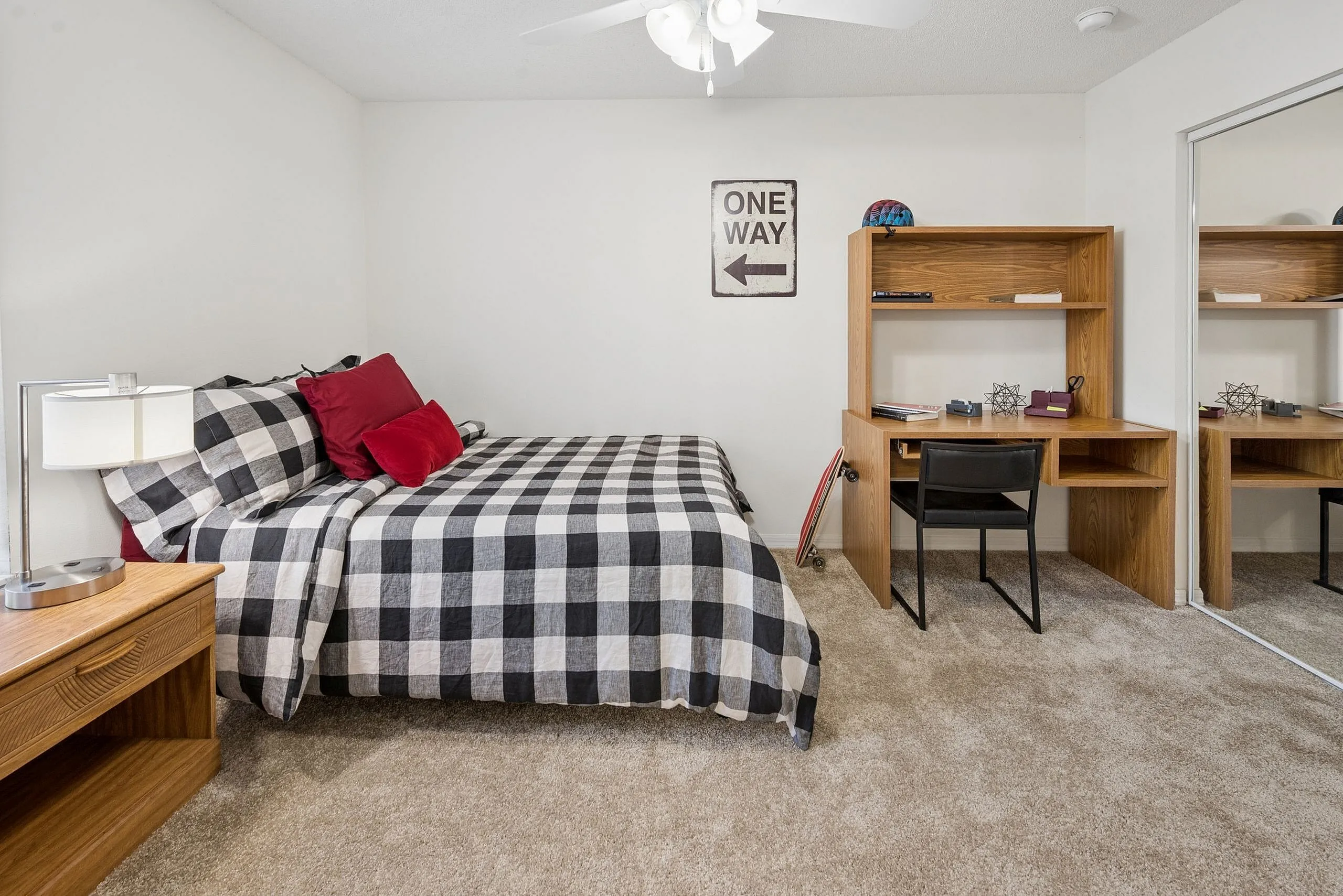 Cozy bedroom with stylish checkered bedding, modern wooden desk, and warm lighting, perfect for relaxation and productivity.