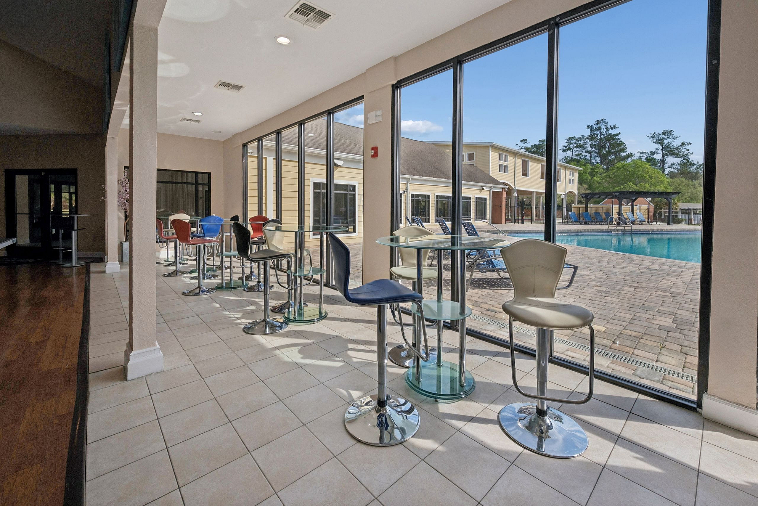 Modern community space with stylish bar seating and floor-to-ceiling windows offering a scenic pool view.