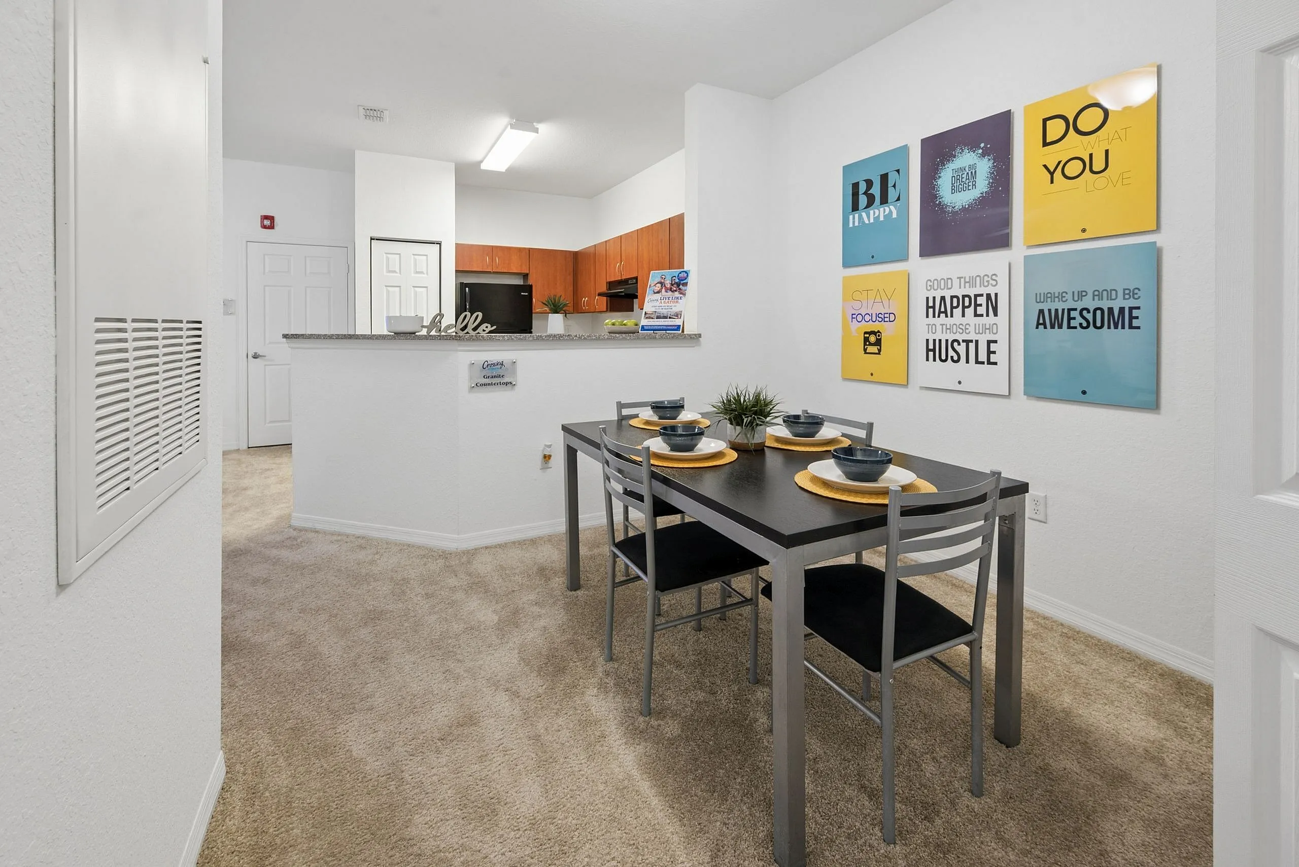 Modern apartment dining area with sleek table set for four, open kitchen, and motivational wall art for an inspiring living space.