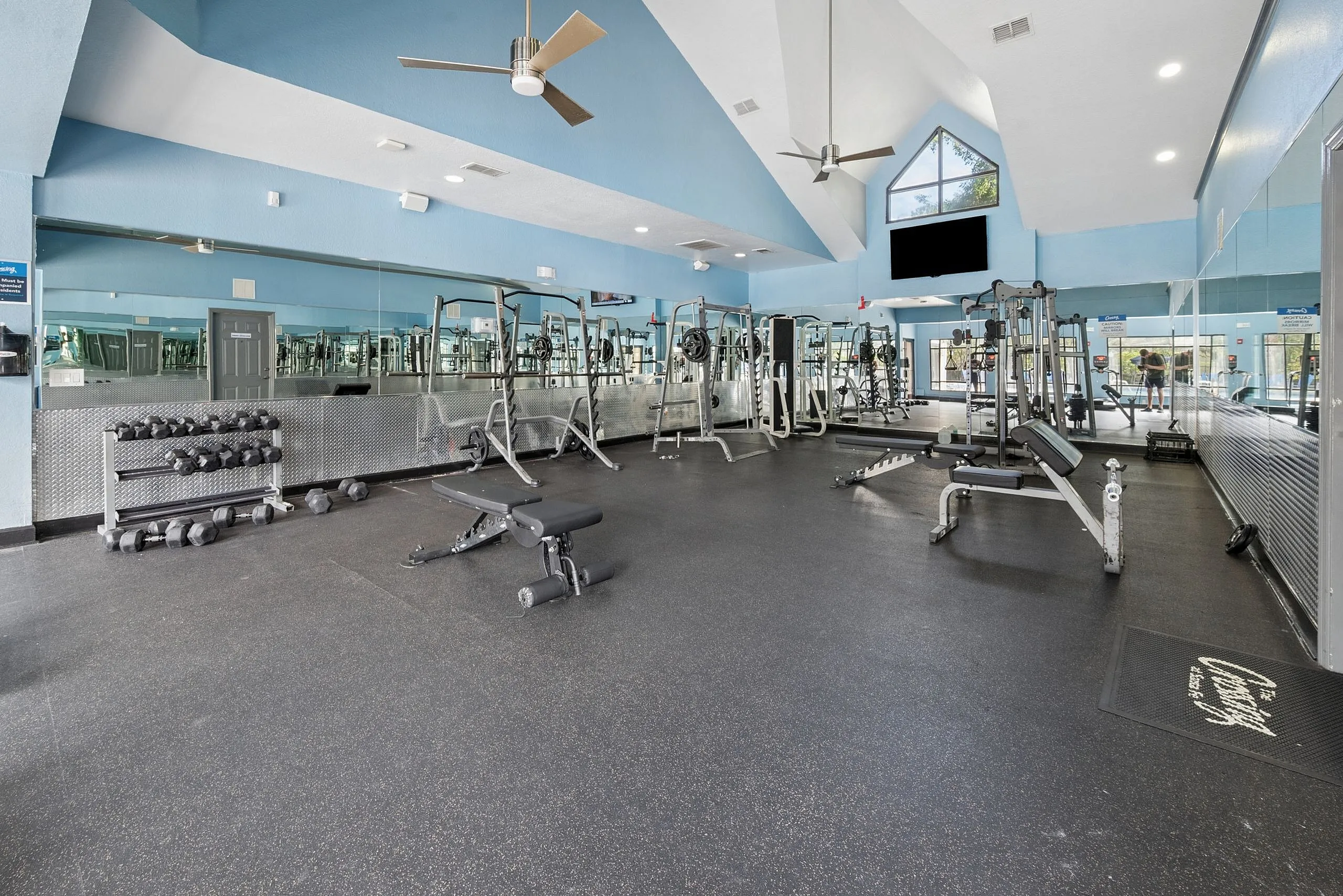 Spacious and modern apartment gym featuring state-of-the-art fitness equipment, natural lighting, and a sleek mirrored wall.