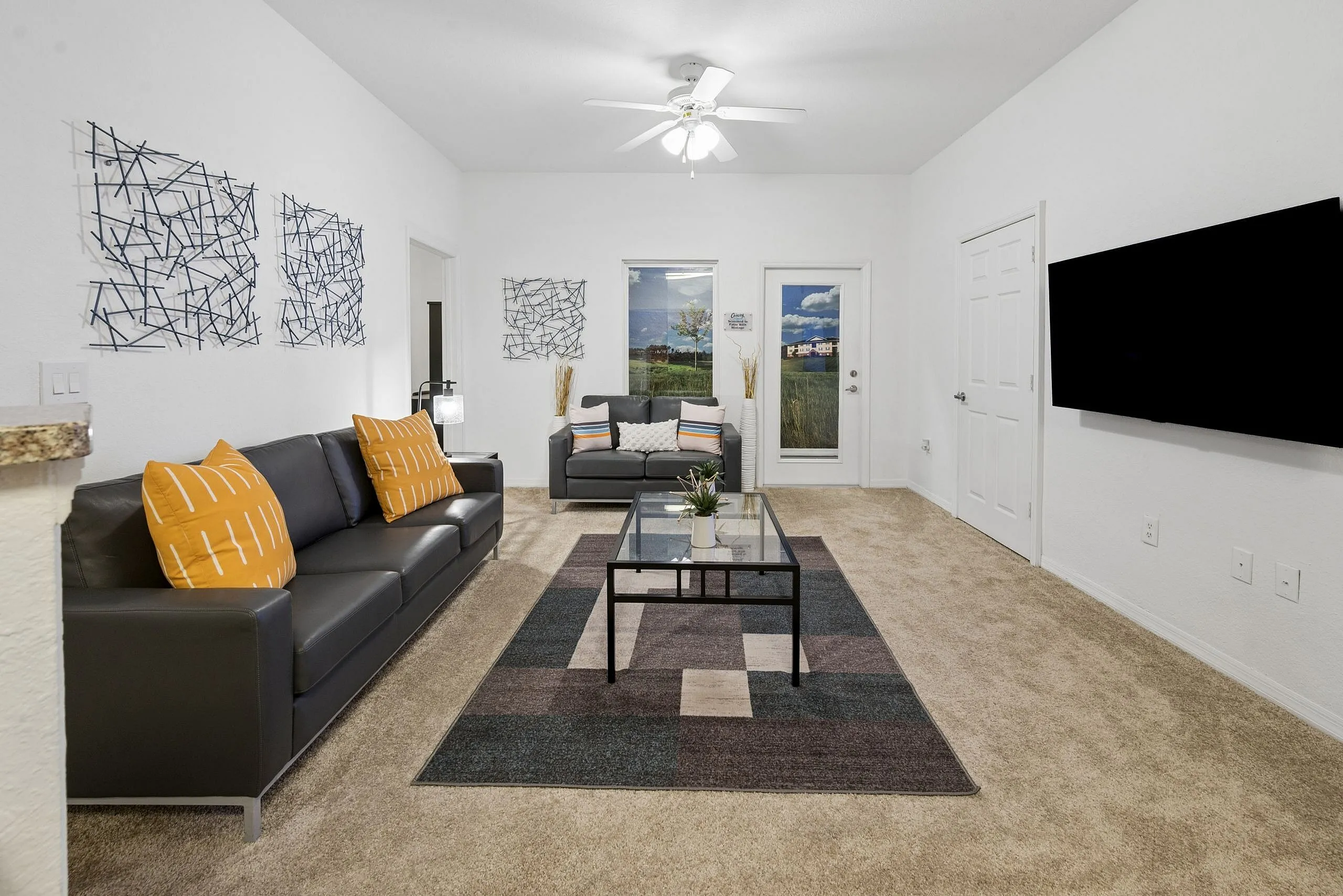 Modern living room with sleek gray sofas, vibrant orange pillows, contemporary wall art, and a stylish glass coffee table on a patterned rug, creating a welcoming and chic atmosphere.