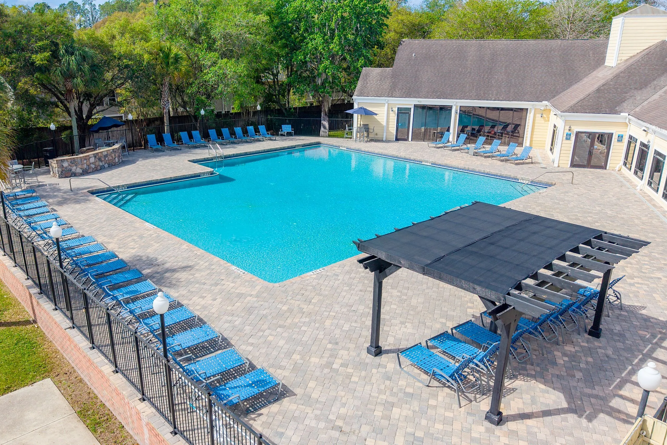 Inviting outdoor pool area with ample seating, shaded pergola, and lush green surroundings, perfect for relaxation and leisure.