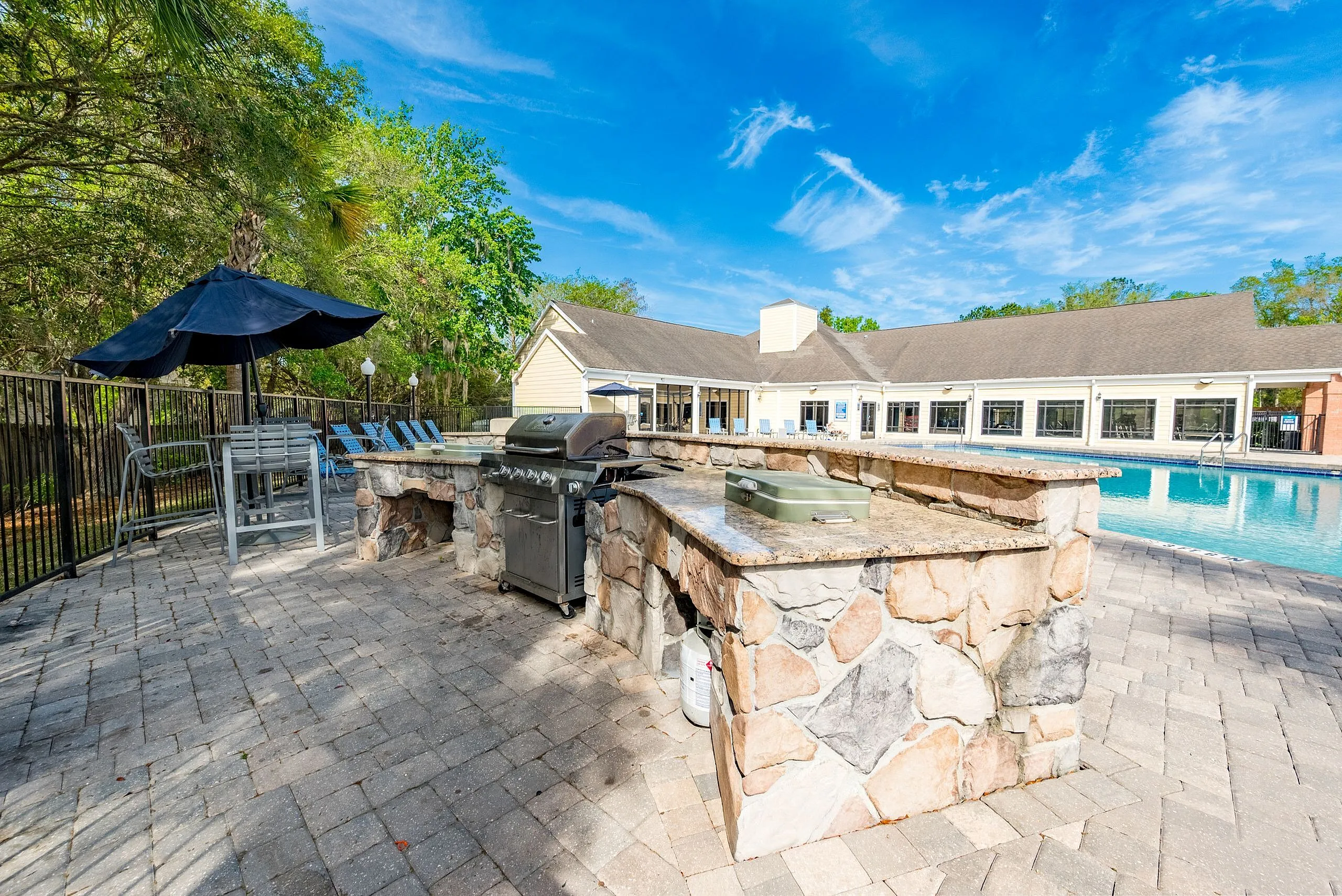 Elegant outdoor patio featuring a stylish barbecue grill and seating area adjacent to a sparkling swimming pool with lush greenery.