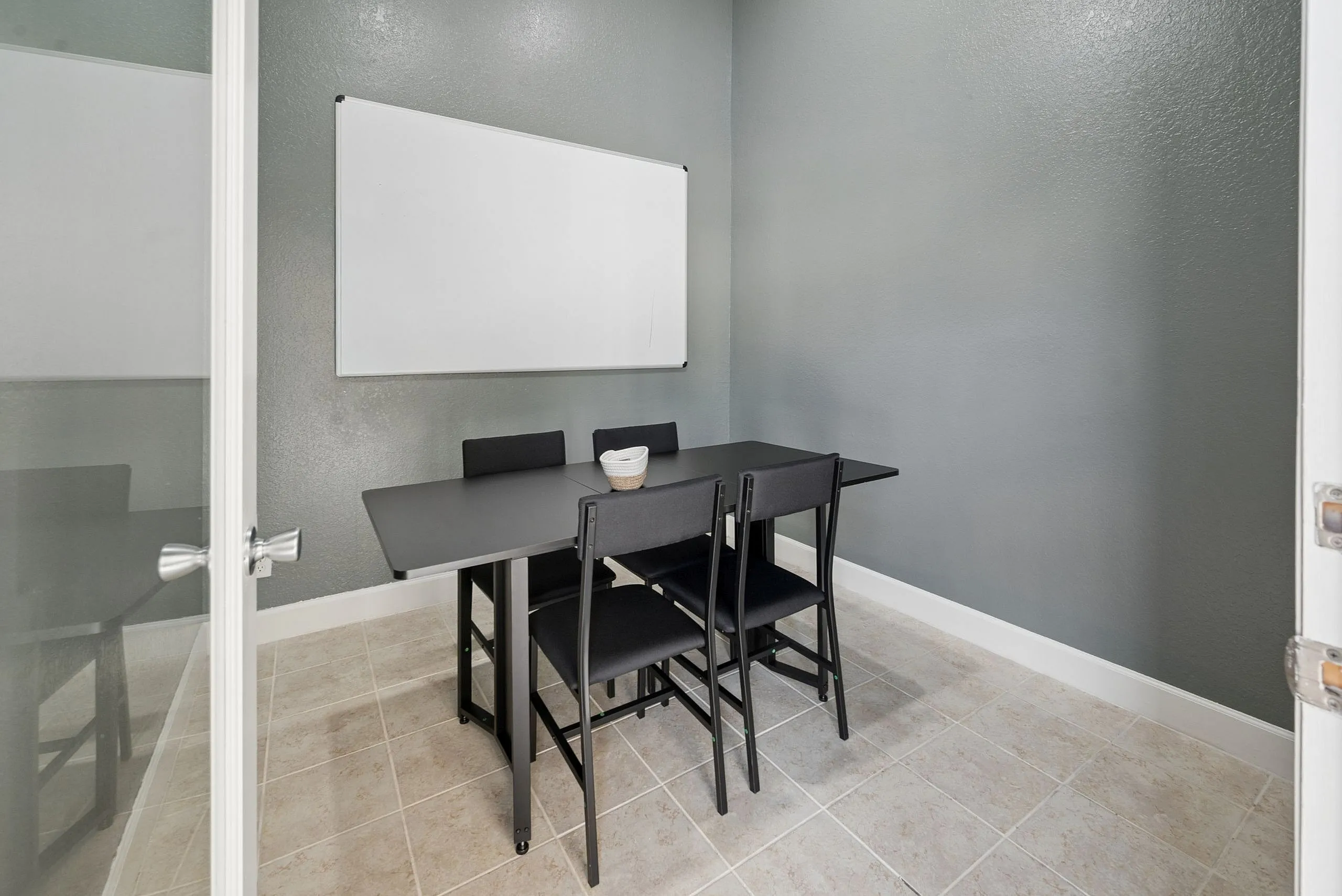 Modern conference room with sleek black table, four chairs, and a whiteboard on a stylish gray wall.