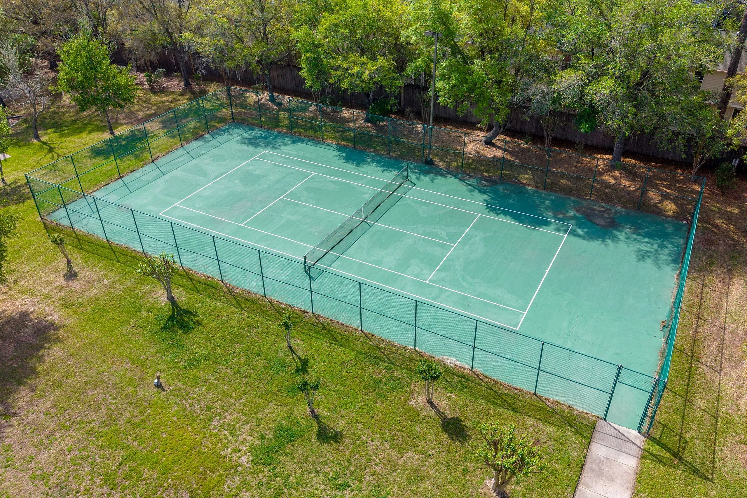 Lush green tennis court surrounded by trees, perfect for outdoor recreation and community sports.