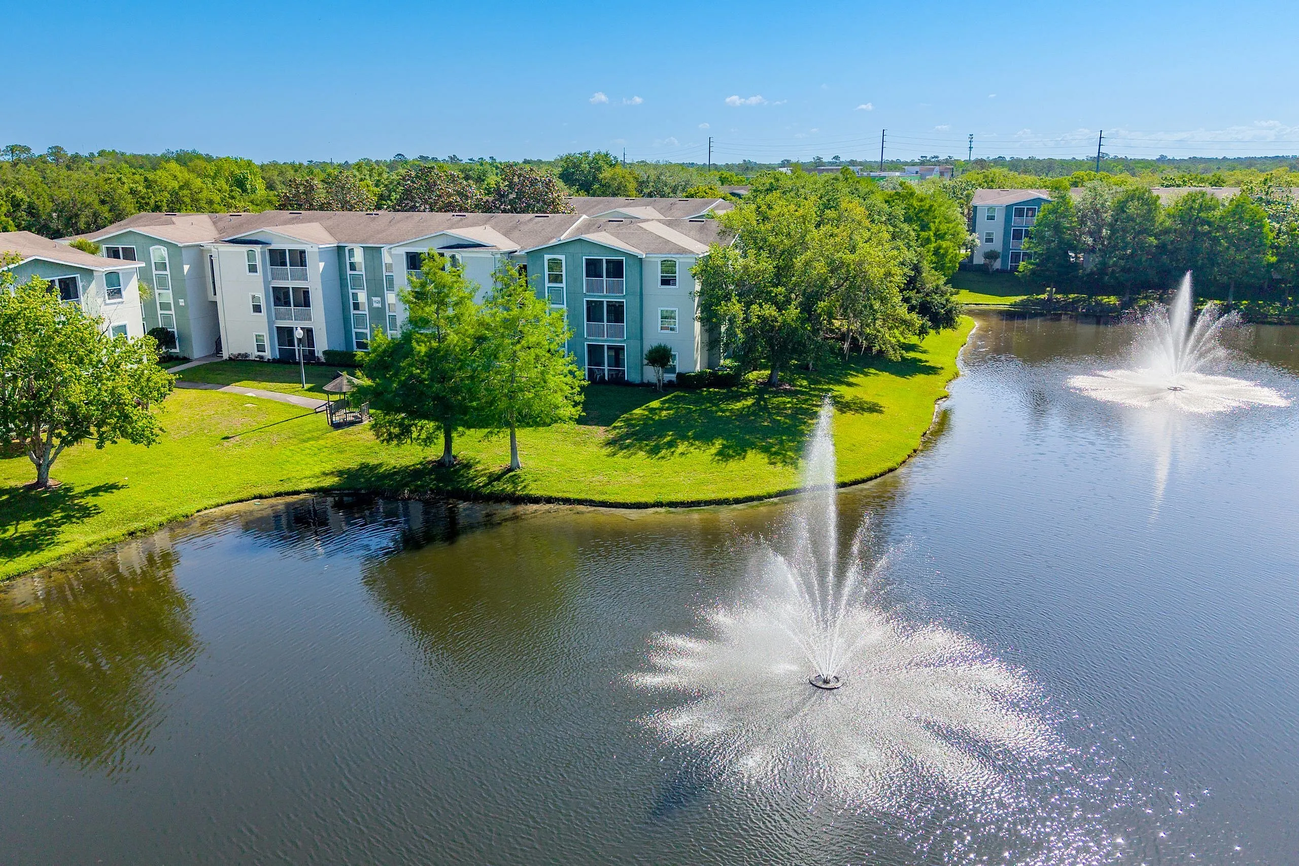 Picturesque apartment complex surrounded by lush greenery and serene water fountains, offering a tranquil living environment.