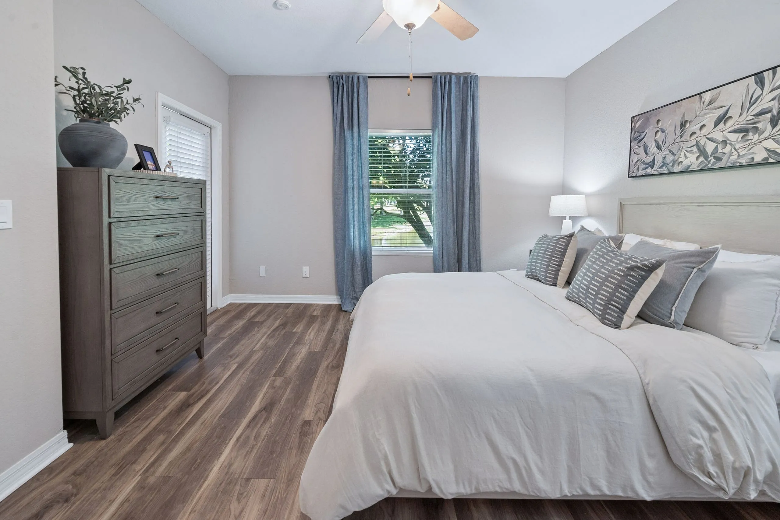Chic bedroom retreat with modern wood flooring, elegant bedding, and a large window offering serene garden views.