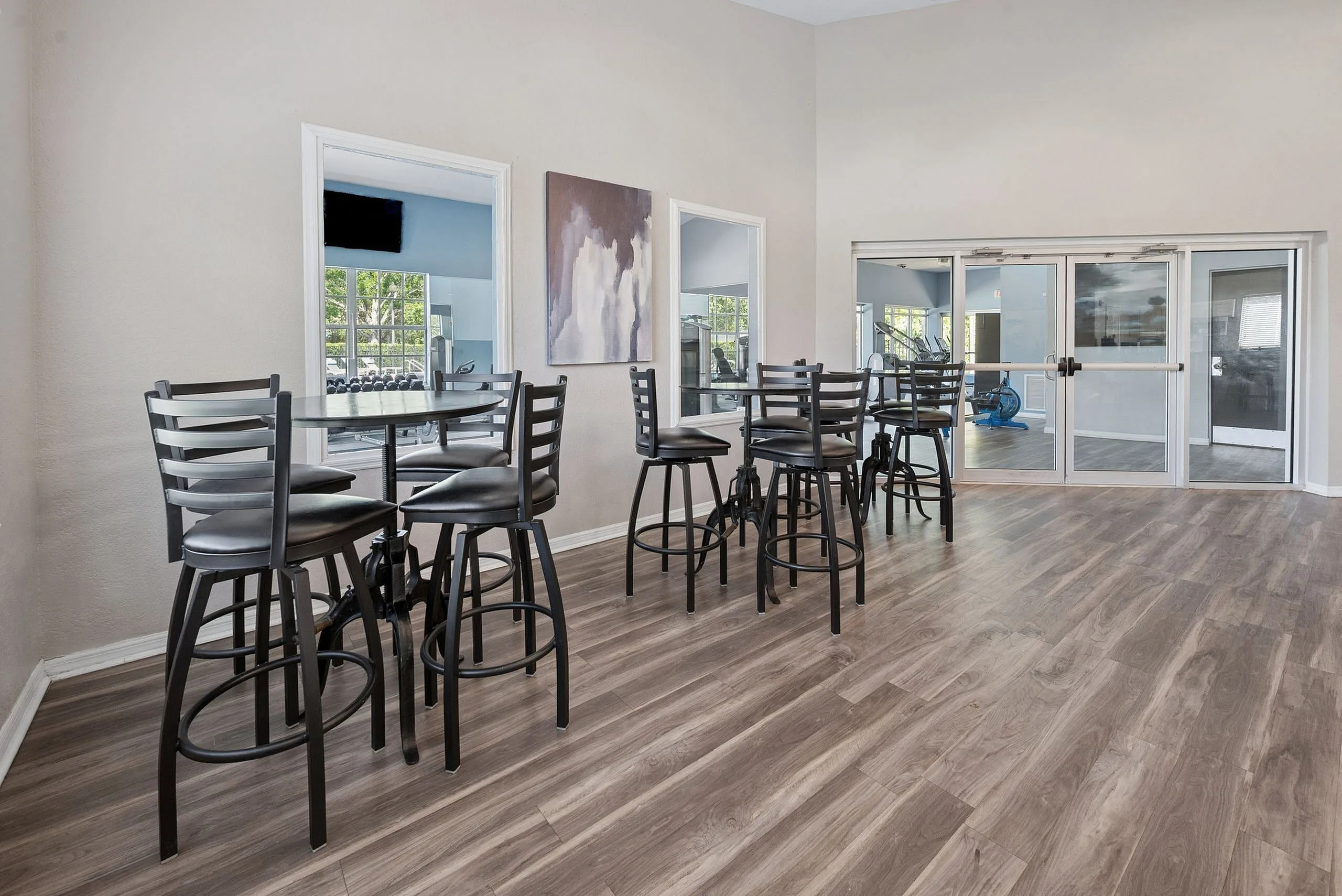 Elegant lounge area featuring modern high-top tables and chairs, with sleek hardwood flooring and large windows overlooking a lush green view.
